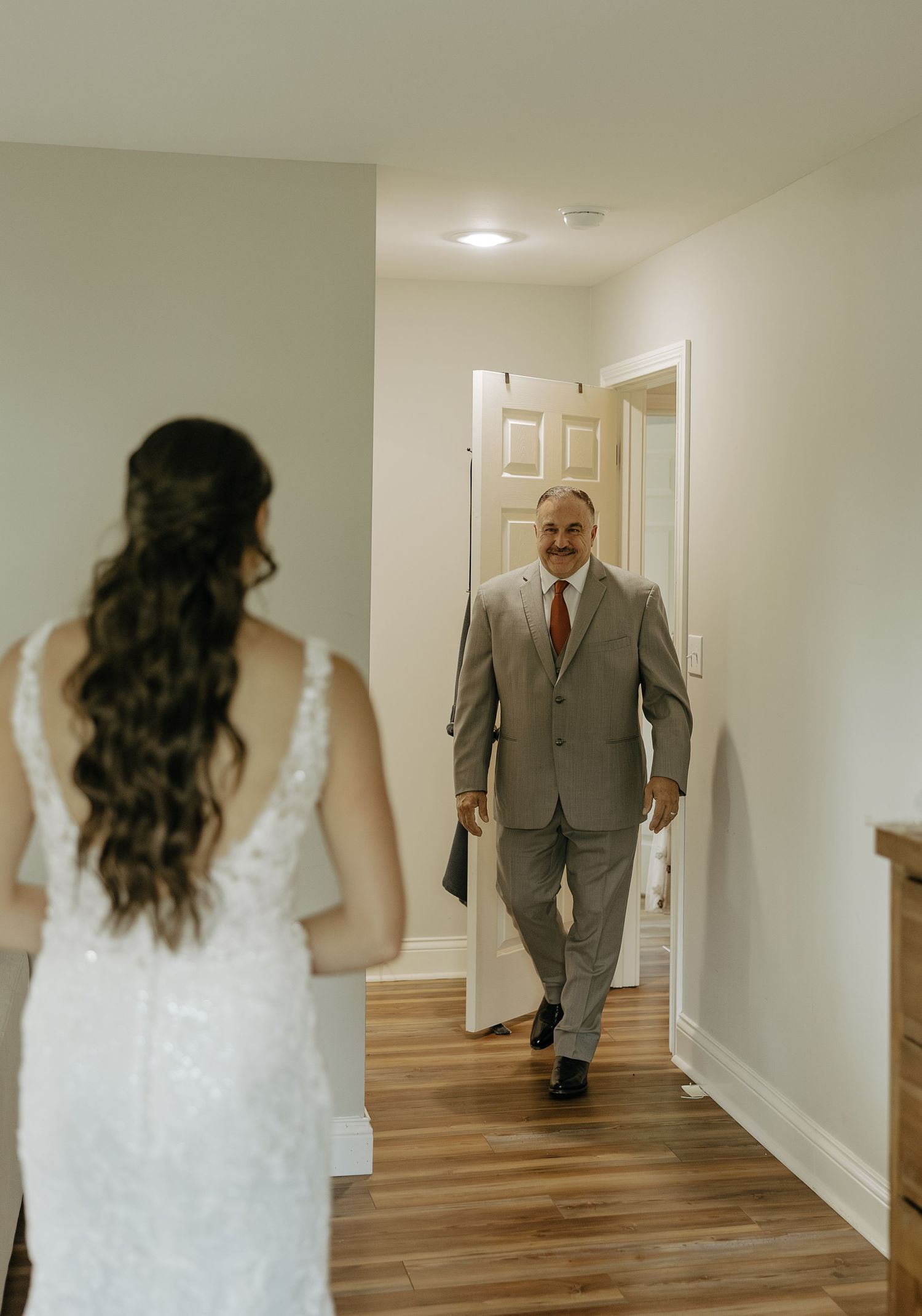 Wedding day first look sequence in a bright hallway with white walls and wooden floors.