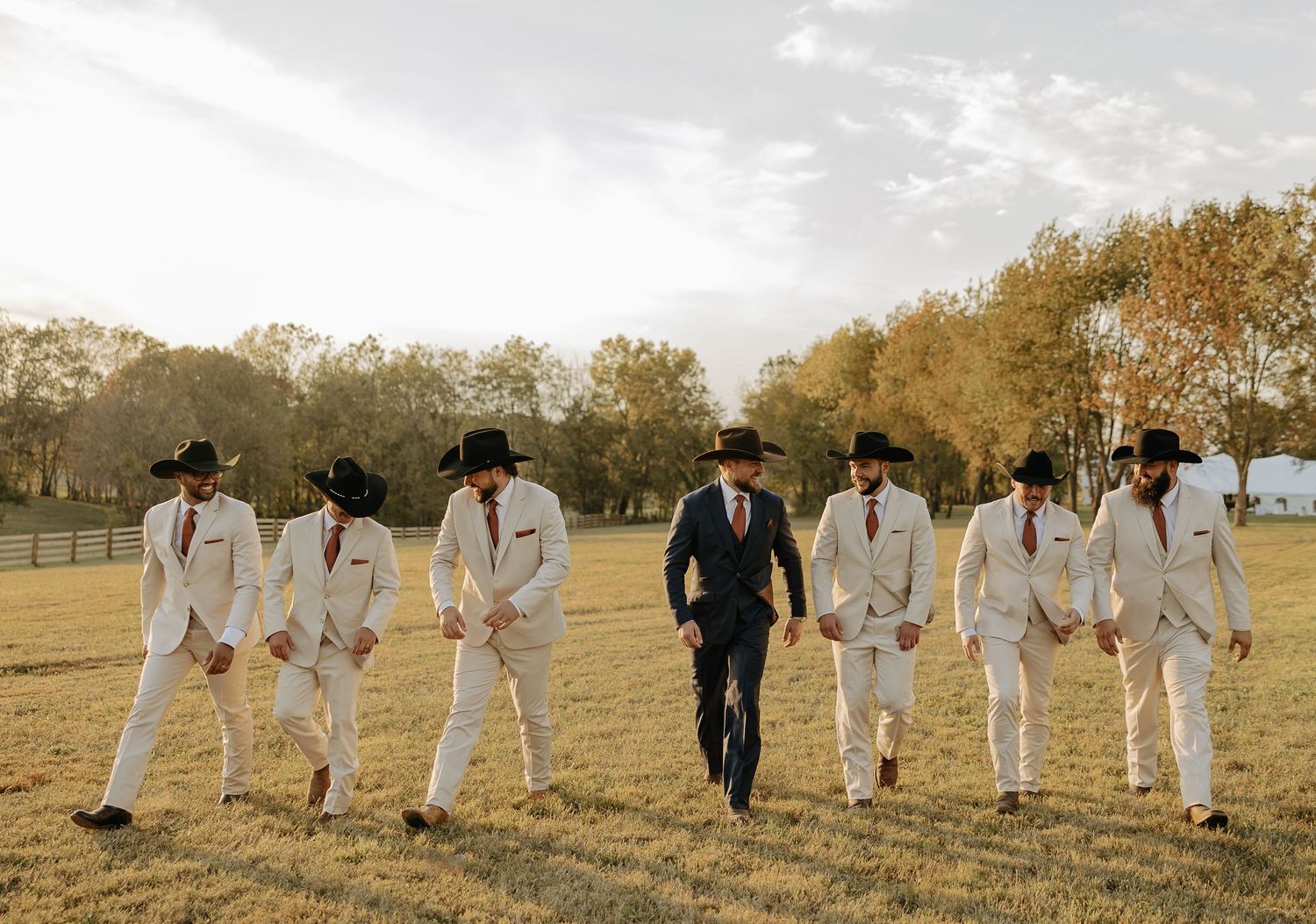 Wedding party walking in line across golden field during sunset.