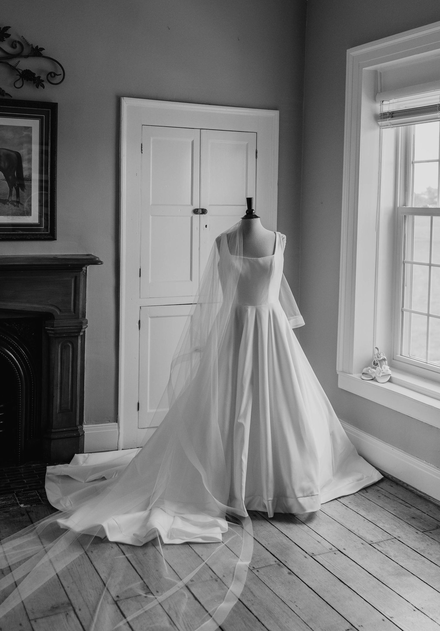 A classic white wedding dress with flowing veil displayed on a mannequin in a sunlit room with hardwood floors.