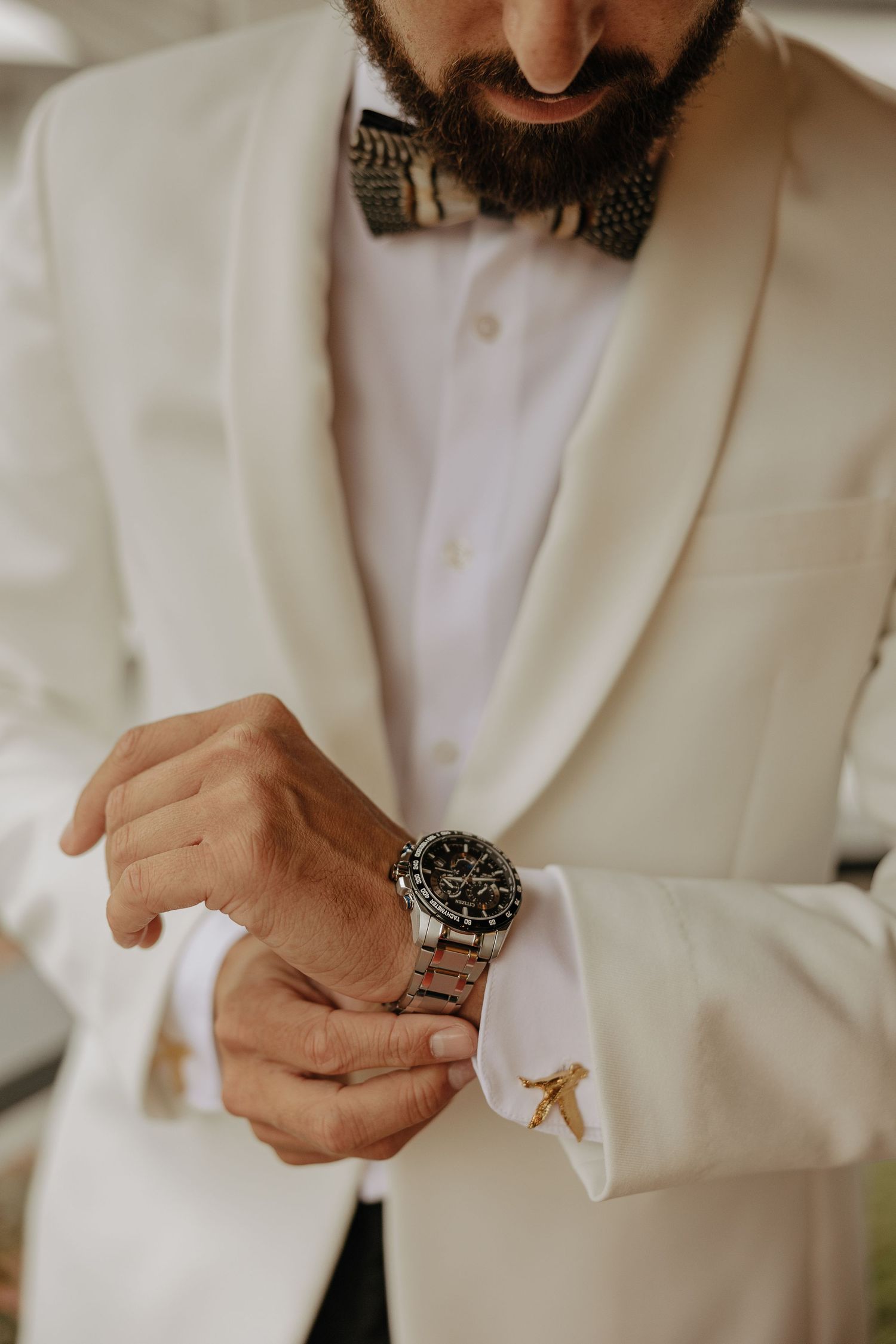 Person in white suit jacket adjusting cufflinks and accessories during wedding preparation.