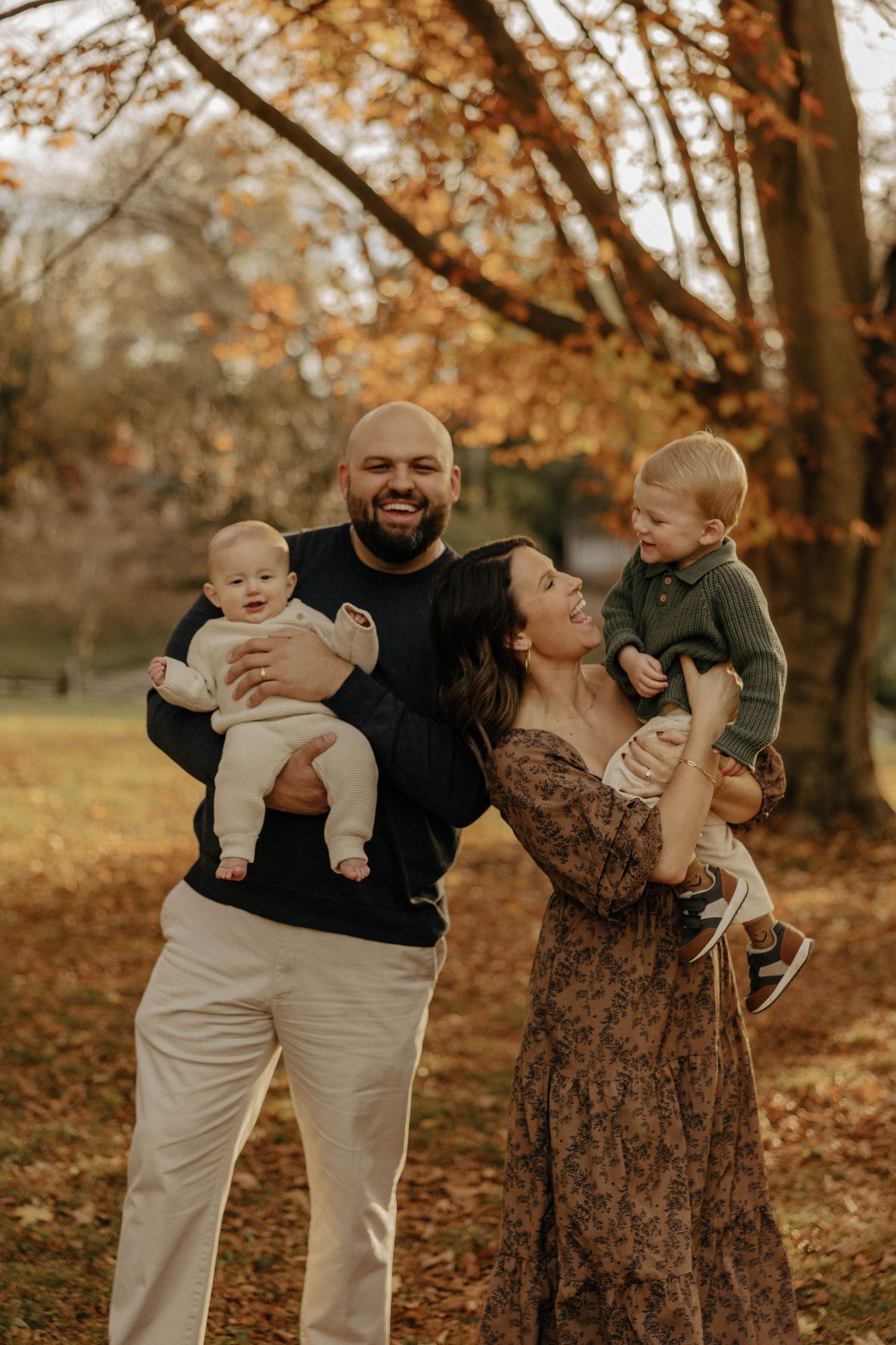 Family shares joyful moments together during autumn photoshoot in a park with fallen leaves.