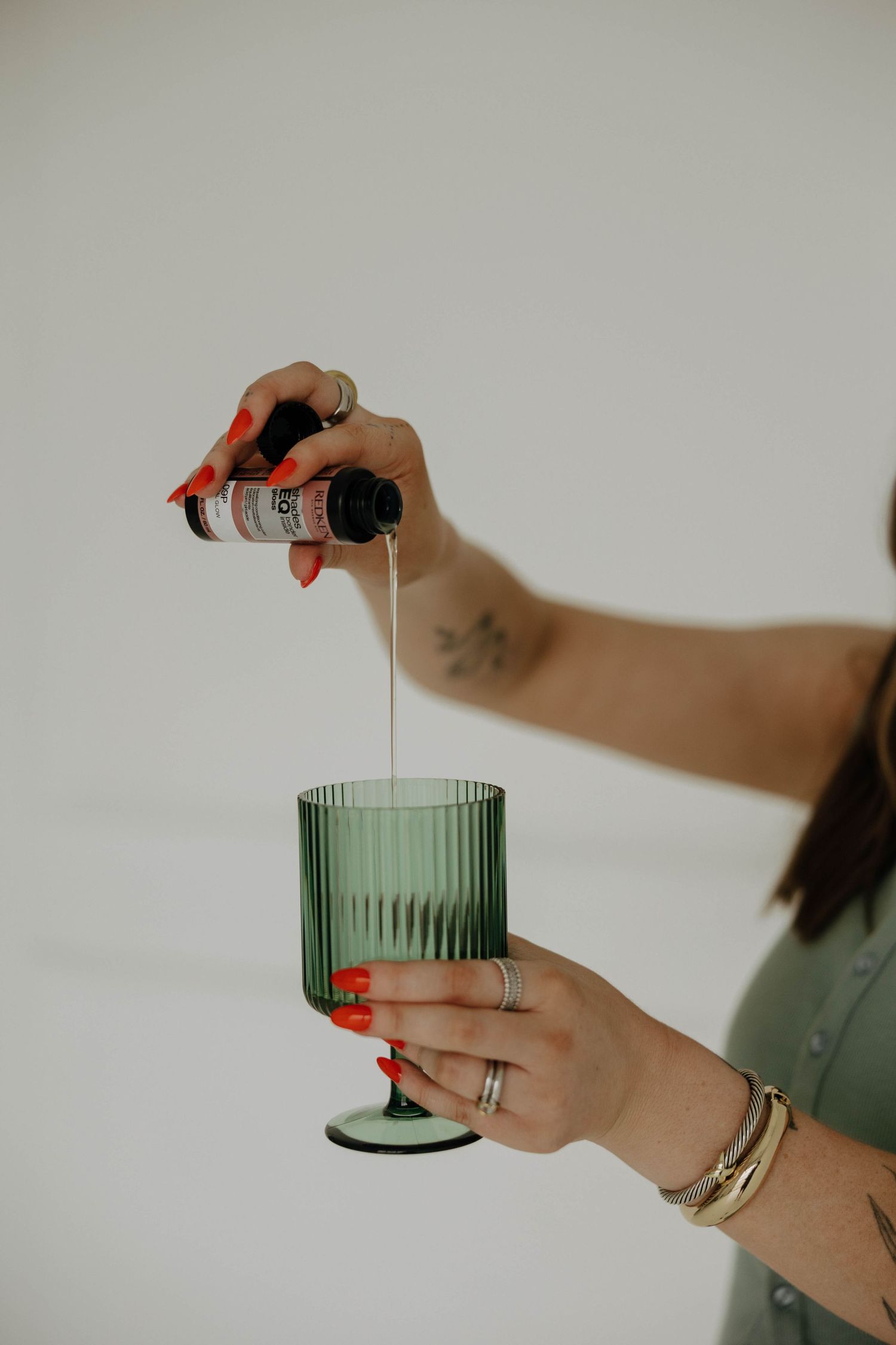 A hand pours clear liquid into a vintage-style green glass with vertical ribbing.
