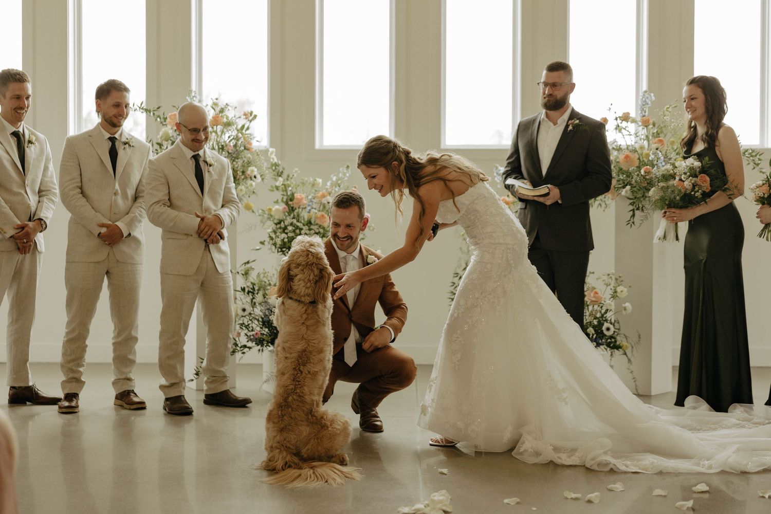 Wedding party poses together in an elegant white columned venue with floral arrangements.
