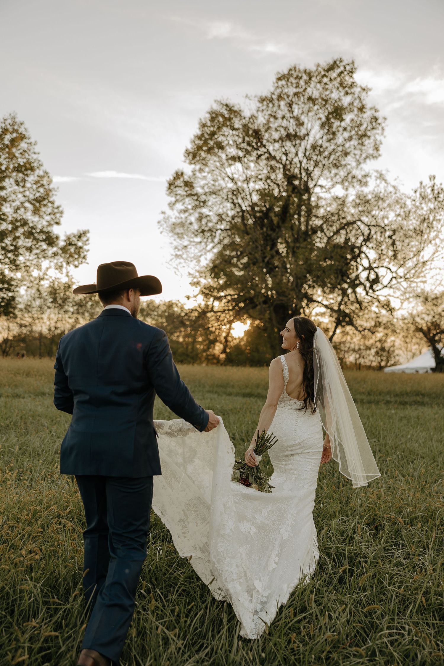 A couple walks through a golden field during sunset at their rustic wedding.