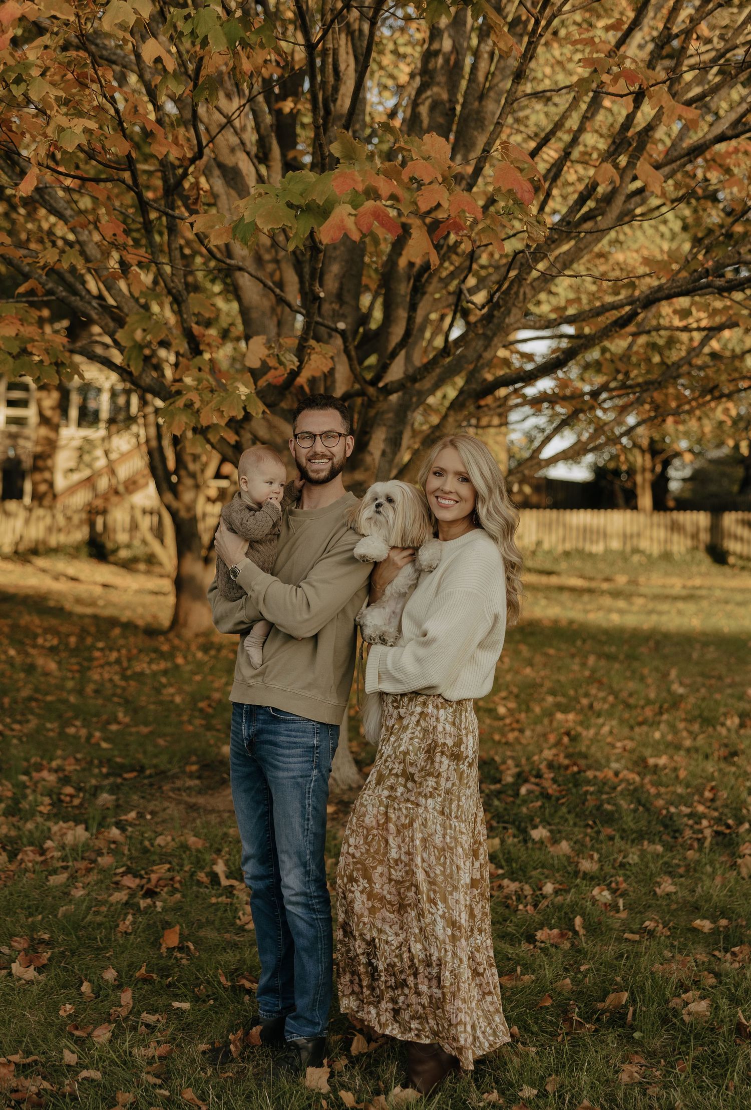 A family portrait under fall trees with golden leaves in the background.