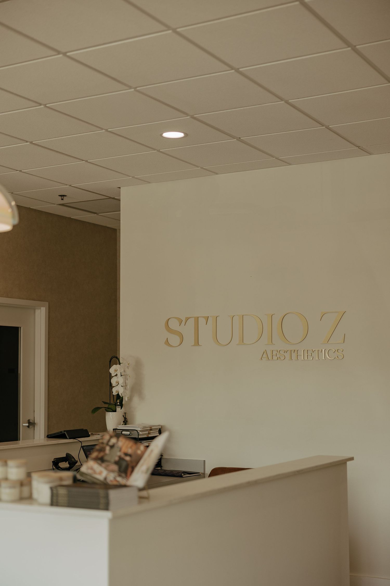 Studio Z Aesthetics reception desk with gold lettering on white wall.
