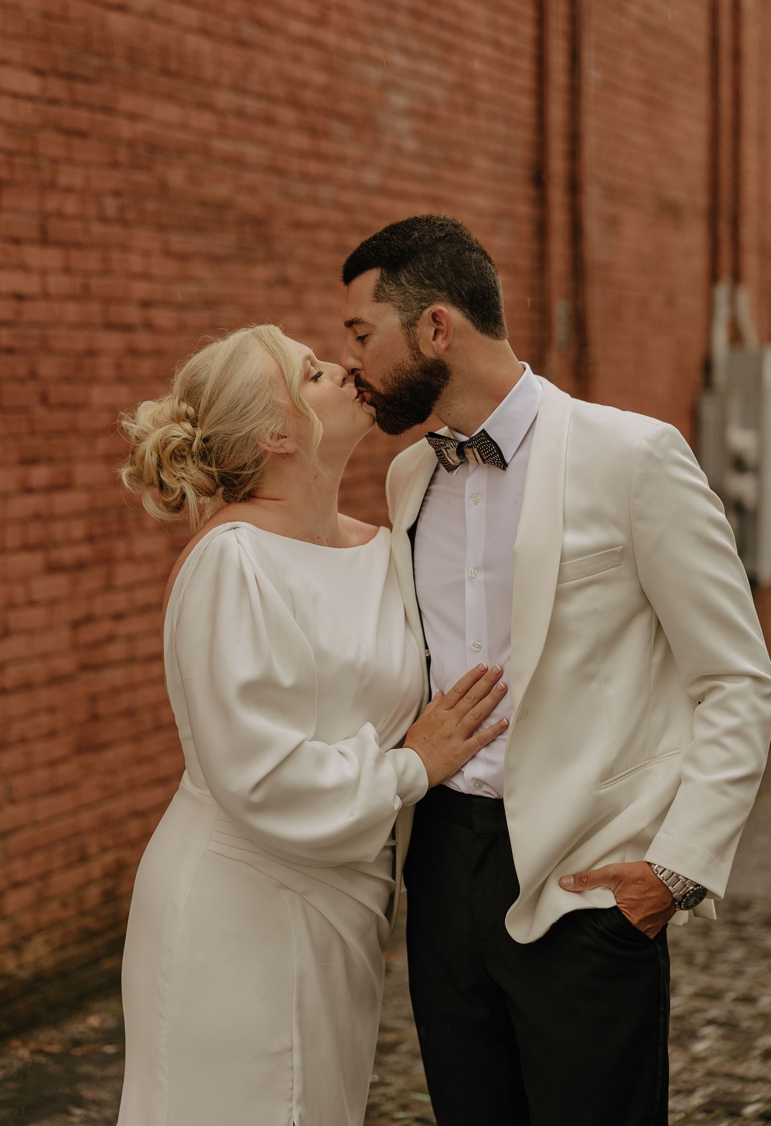 Romantic wedding moment captured against rustic brick wall backdrop.