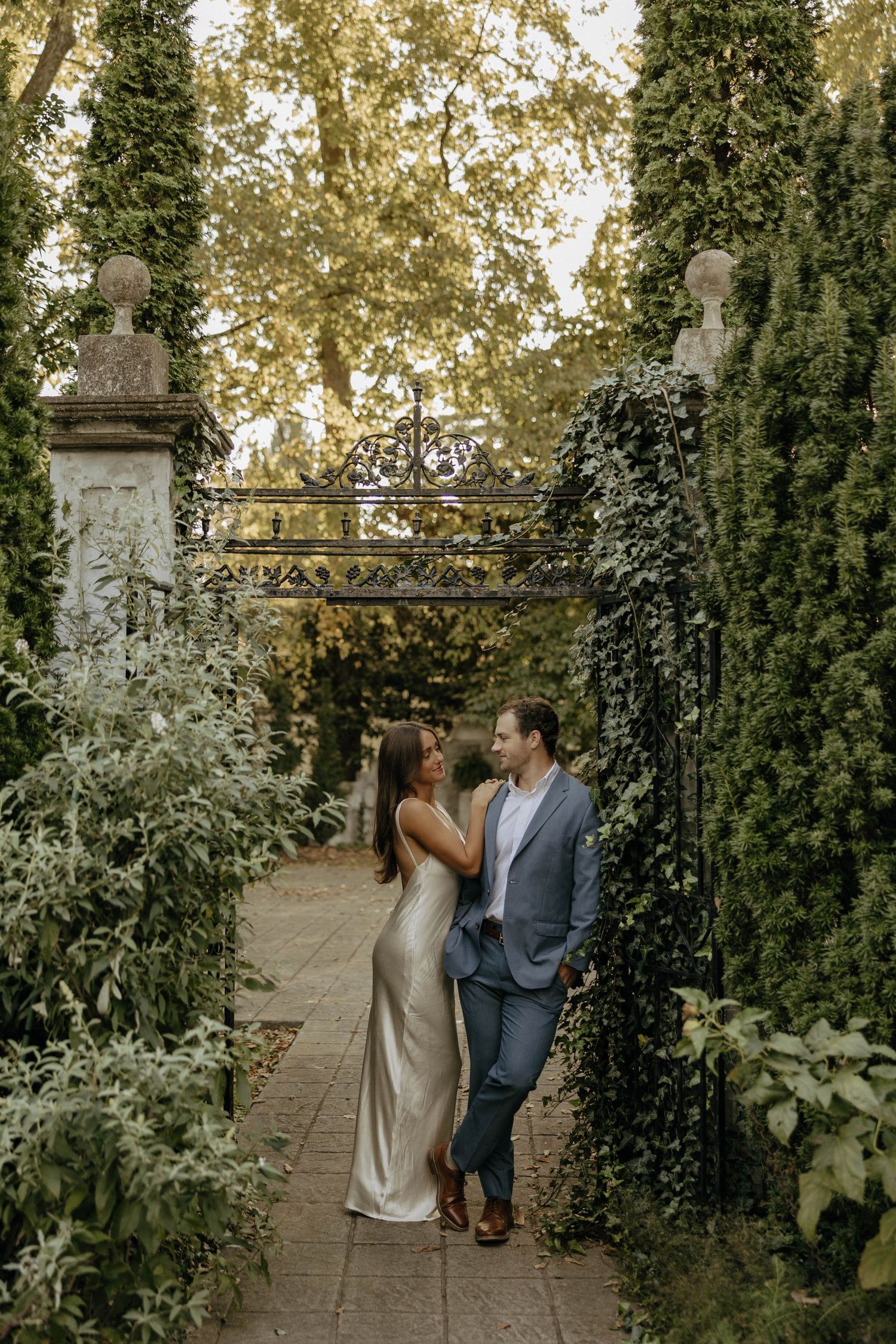 A couple shares a romantic moment among ivy-covered pillars in a garden setting.