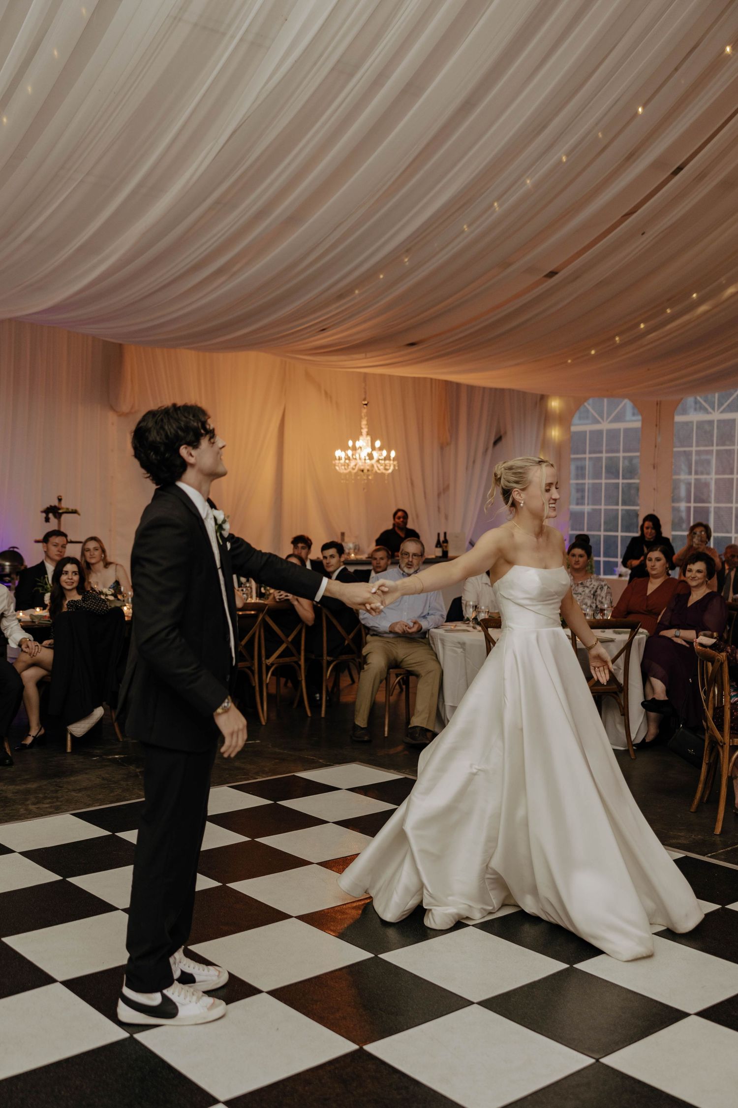 Couple dancing on a black and white checkered floor under a white tent reception.