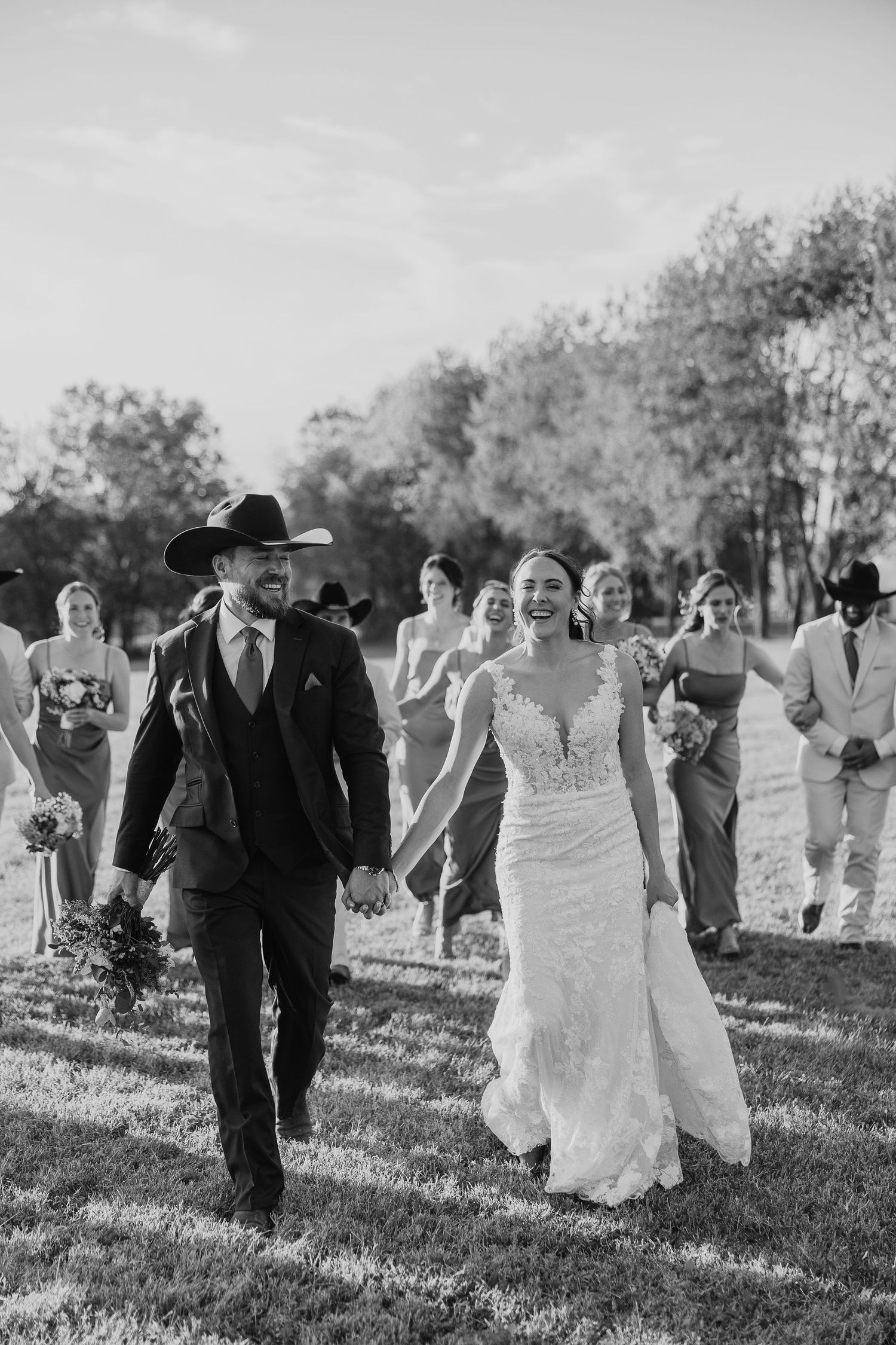 A wedding party walks together across a grassy field in black and white photography.