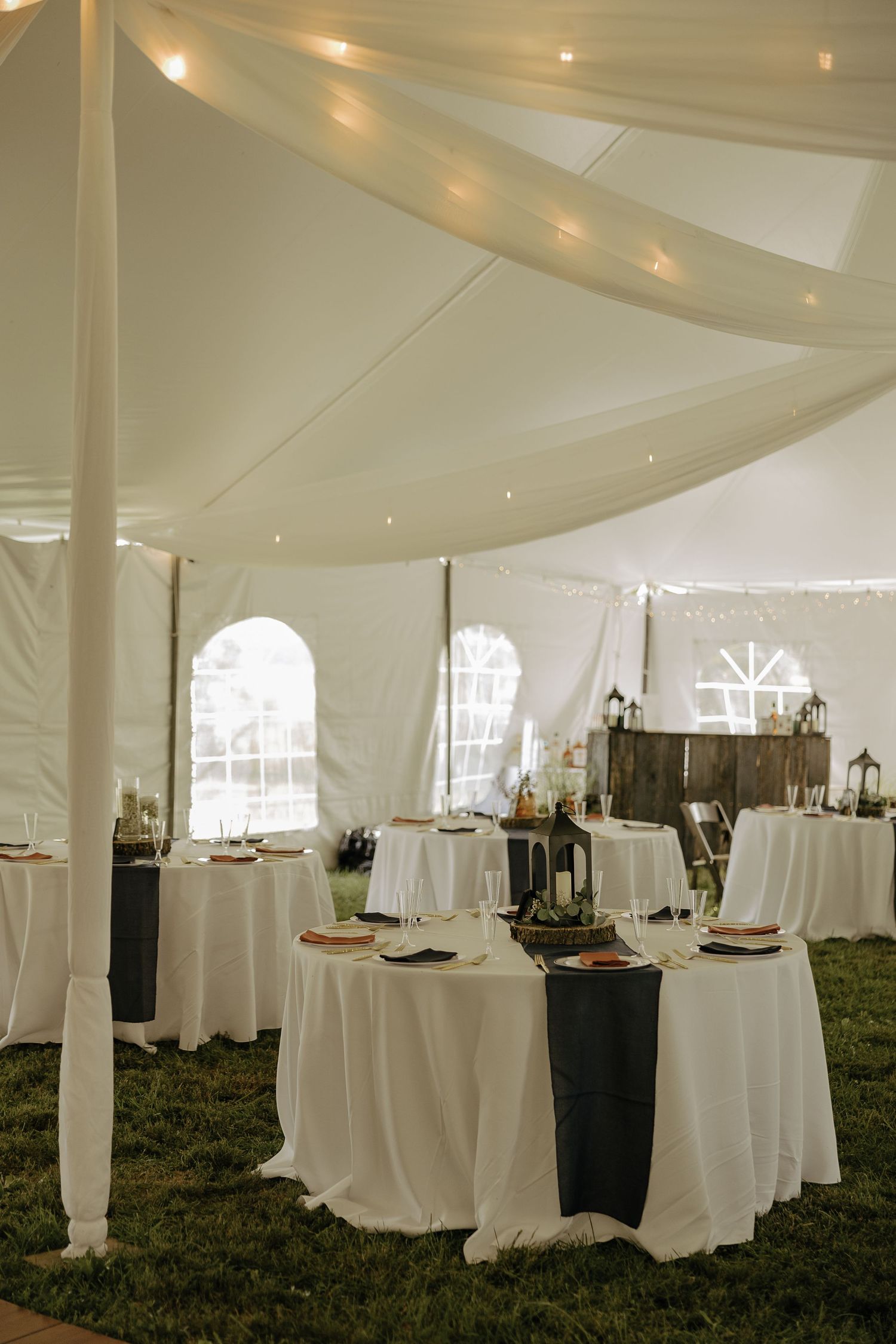Elegant white wedding reception tent with round tables and string lights.