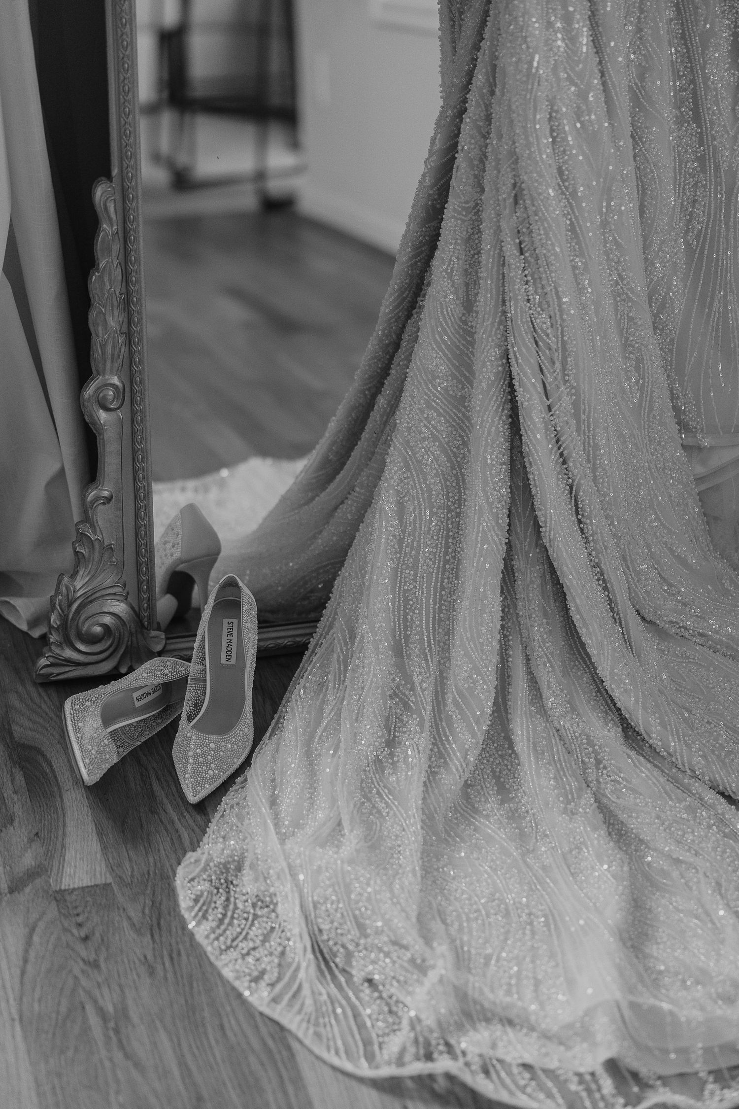 Close-up details of an elegant wedding dress train with intricate lace patterns and delicate embroidery on the floor.