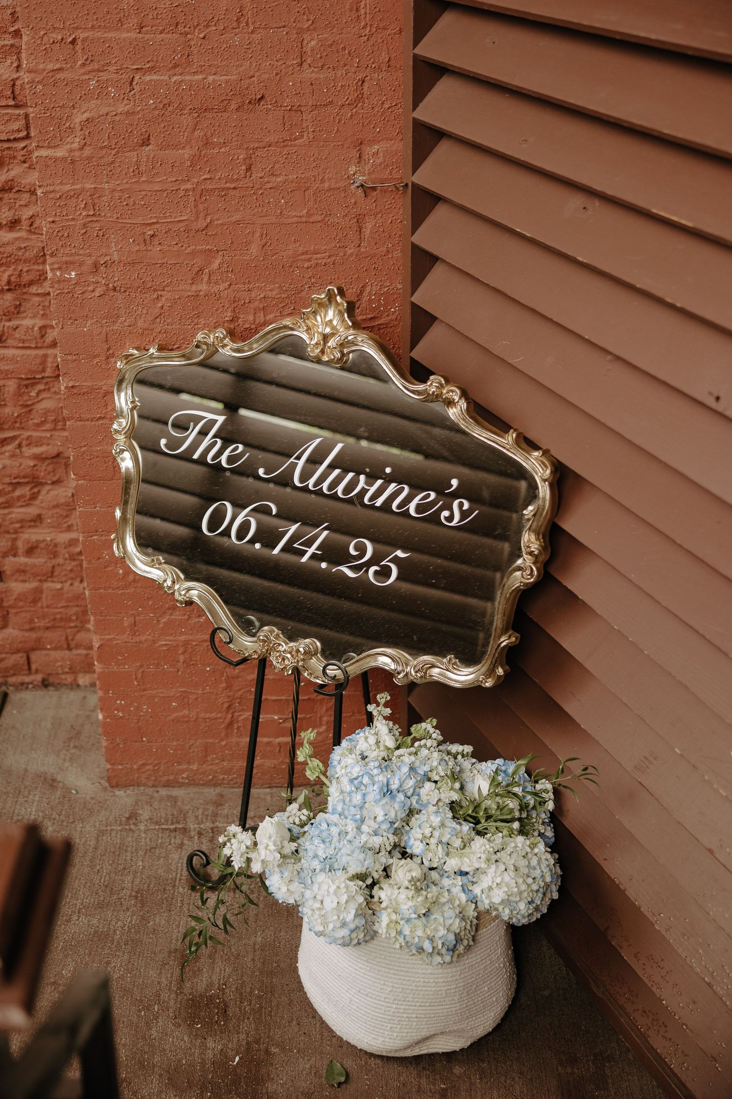 Rustic wedding sign displaying 'The Malone's 06.11.23' with white flowers in a vintage arrangement.