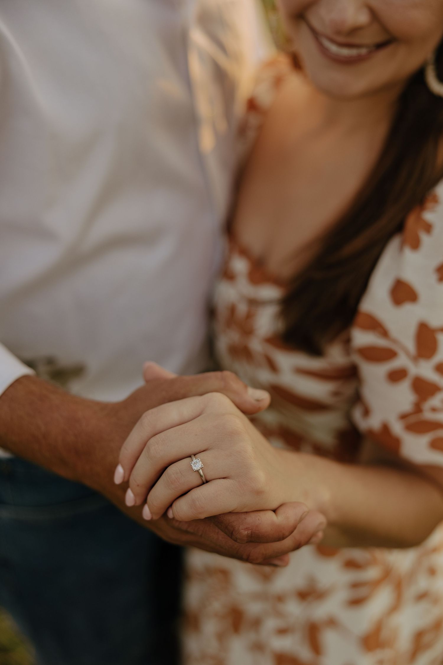 Close-up shot of hands with an engagement ring in warm sunset lighting.