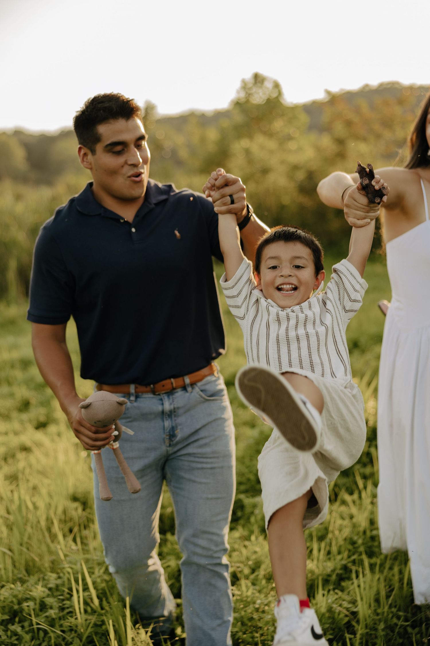 Playful family interaction in a grassy field at sunset.