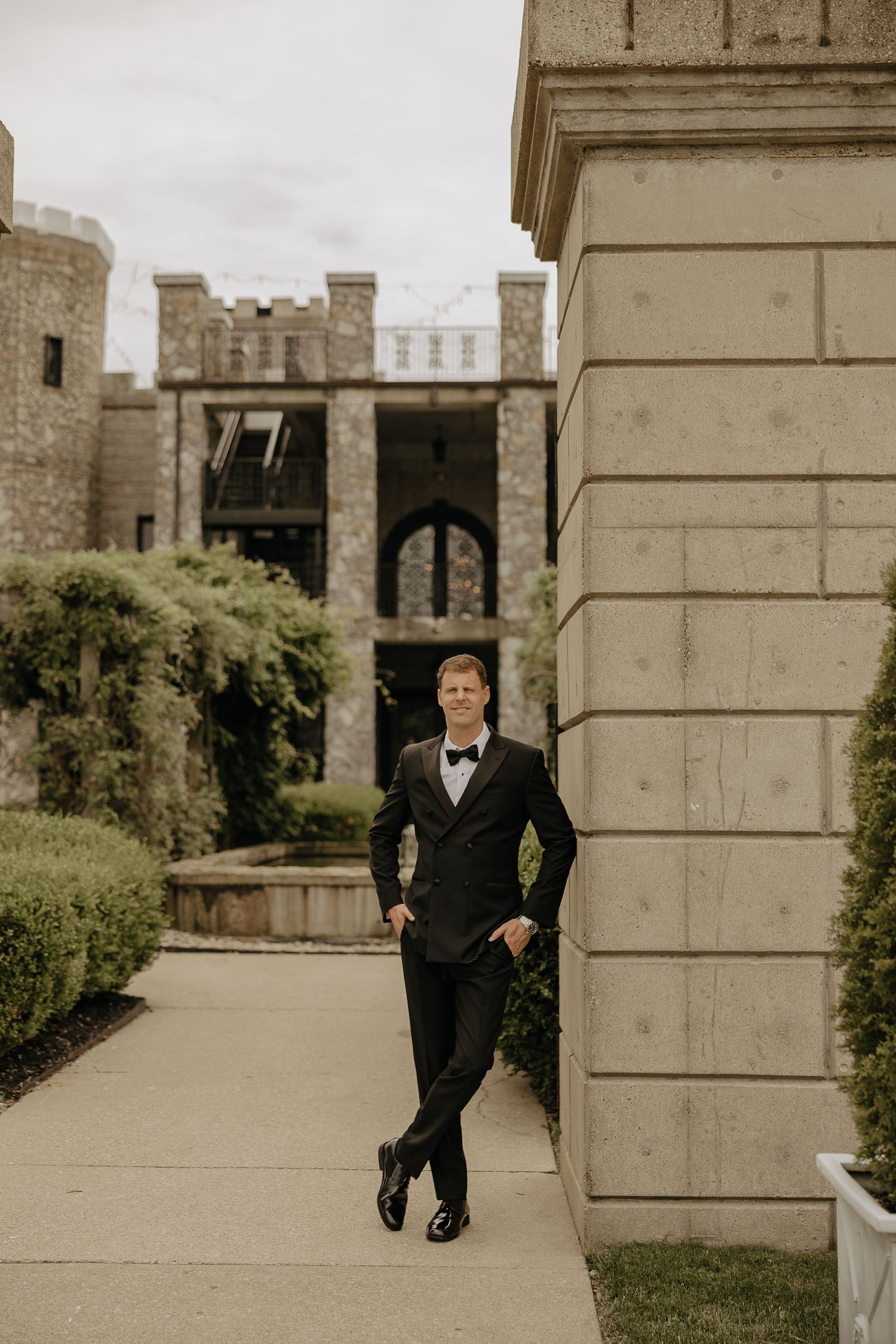 A formal portrait against a stone castle backdrop featuring classic architectural elements.