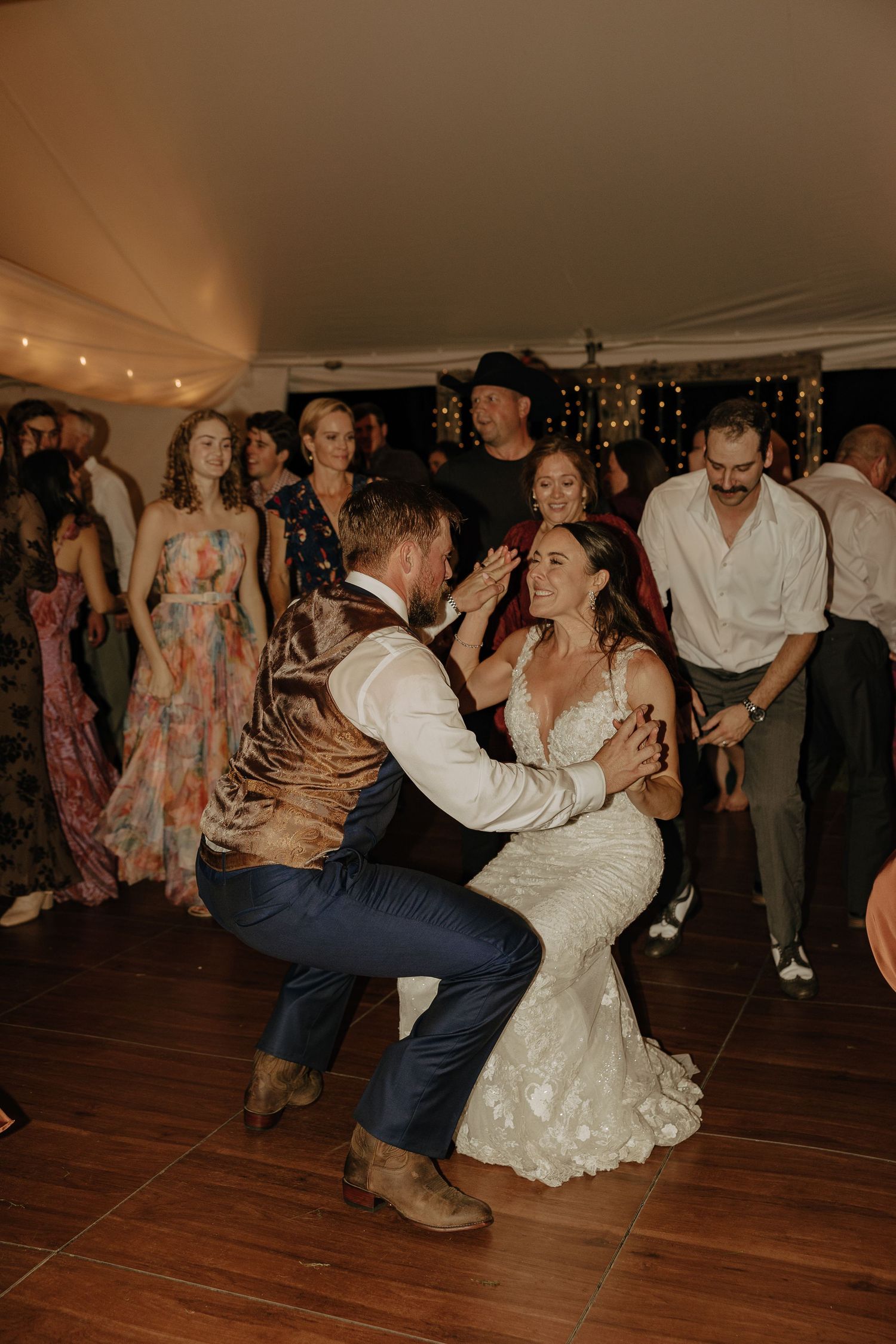 Wedding guests dance energetically on a wooden floor during the reception celebration.