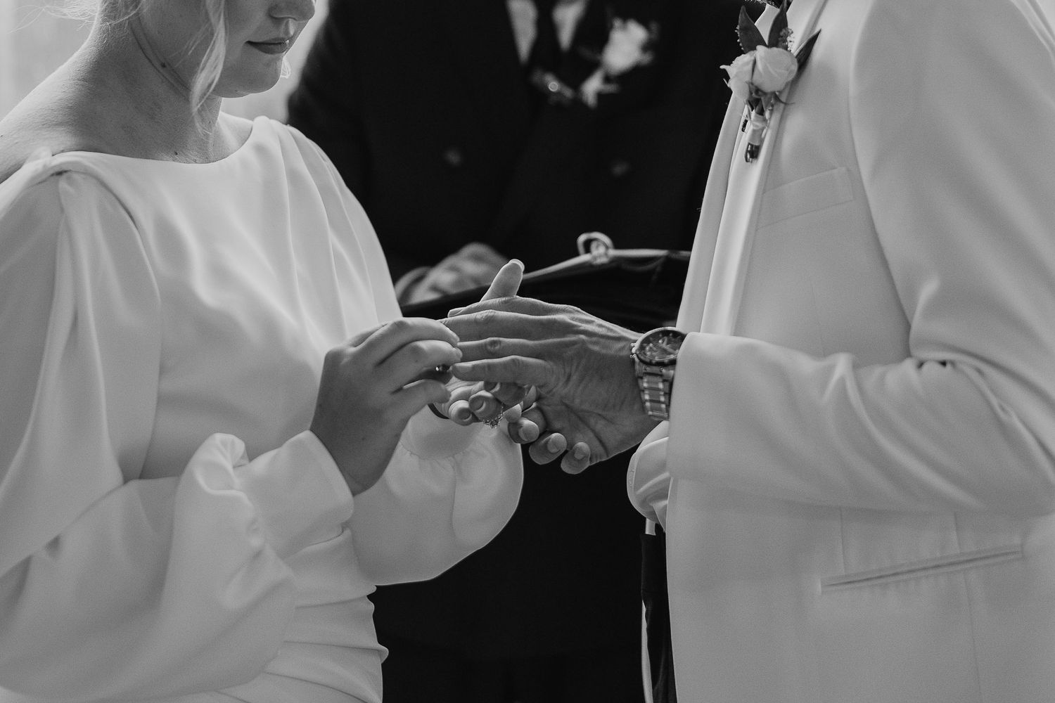Close-up details of wedding ceremony moments in black and white showing hands exchanging rings.
