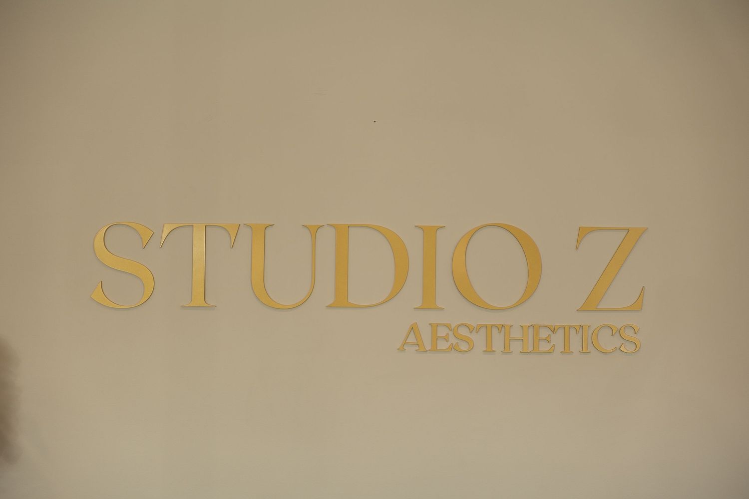 Gold lettering spelling 'STUDIO Z AESTHETICS' on a beige wall.