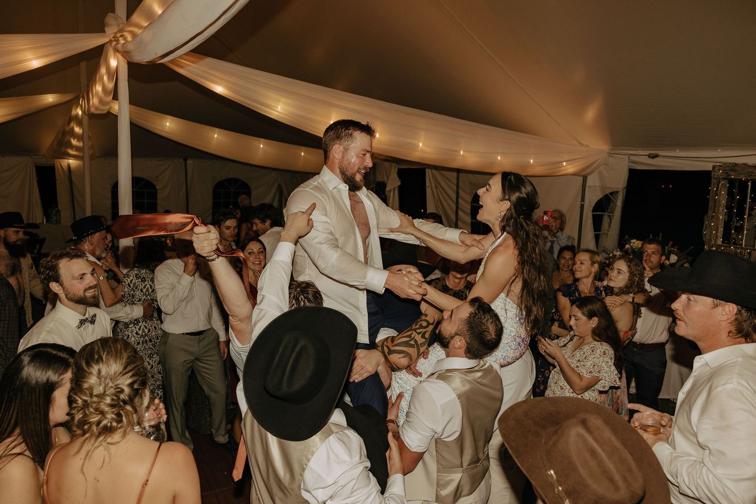 Wedding reception dance floor filled with guests celebrating under warm lighting.