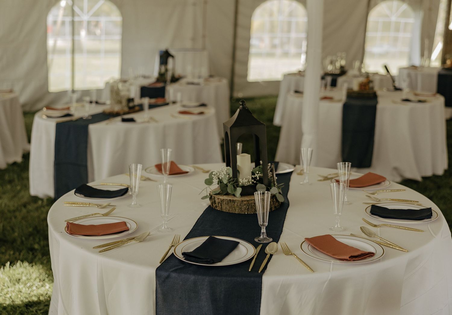 White reception tables set with place settings under an outdoor tent for an elegant wedding.
