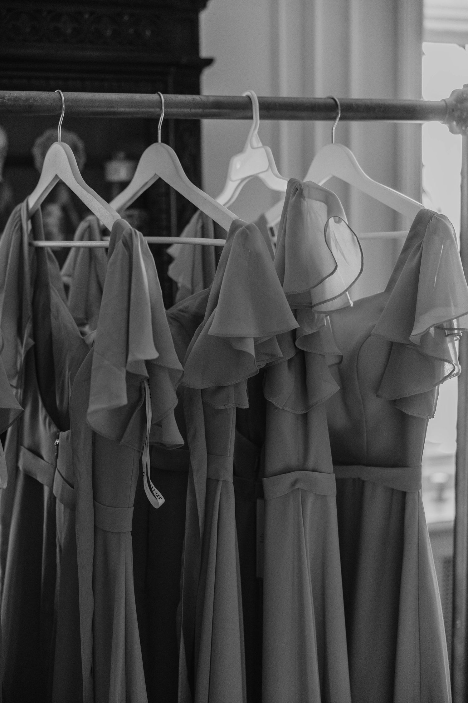 Monochromatic view of clothing rack with formal dresses and garments hanging on hangers in a retail store.