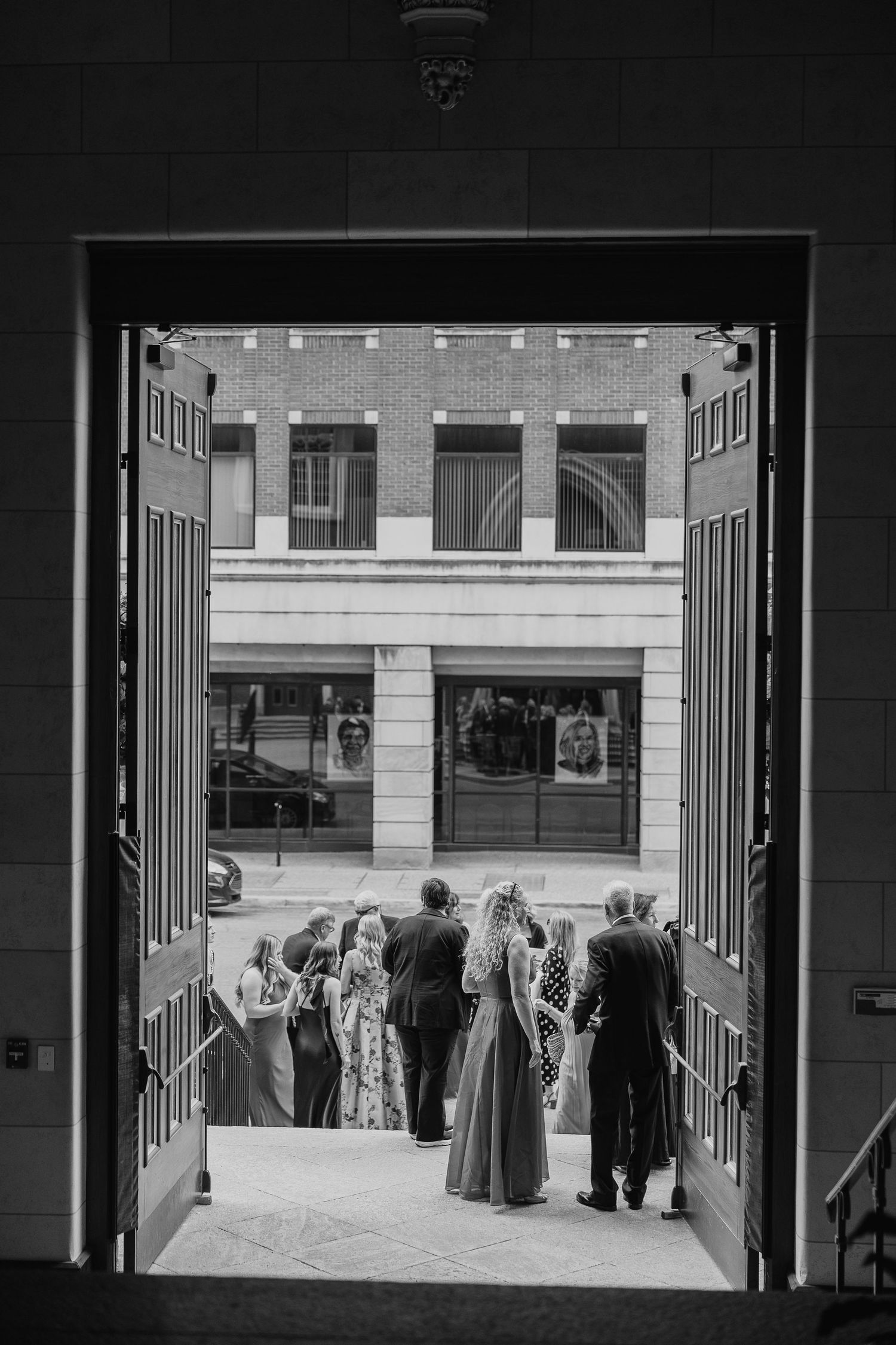 Wedding guests gather outside church doors in black and white urban courtyard photo.