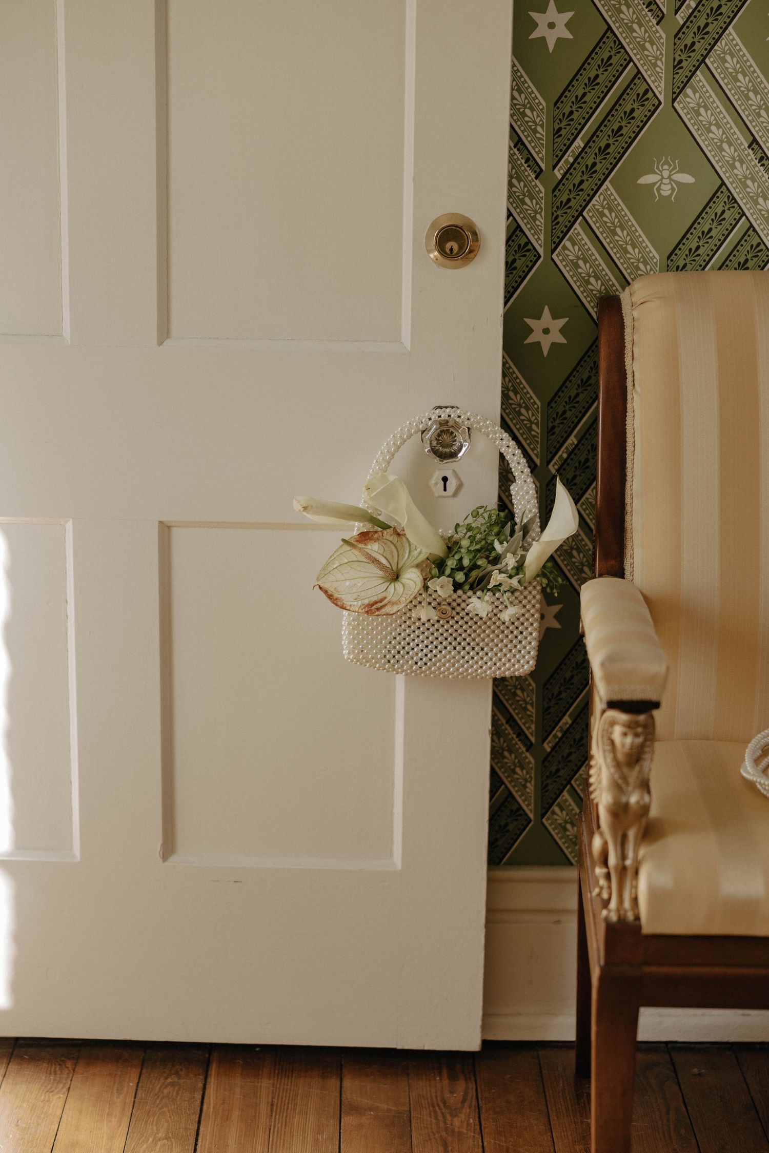 White bridal shoes and floral arrangement displayed on vintage door with green geometric wallpaper.