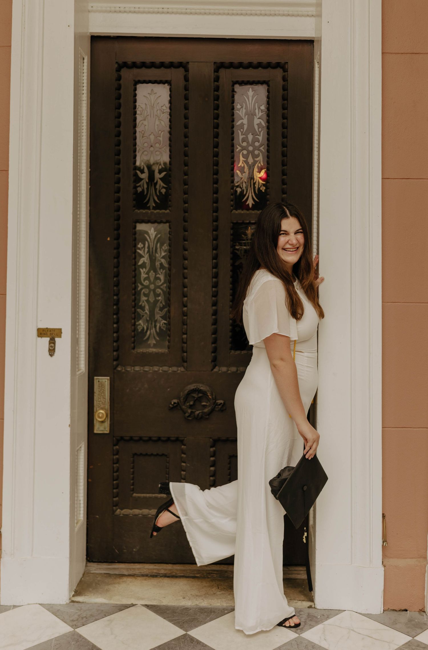 Graduate poses between white pillars in front of ornate double doors.