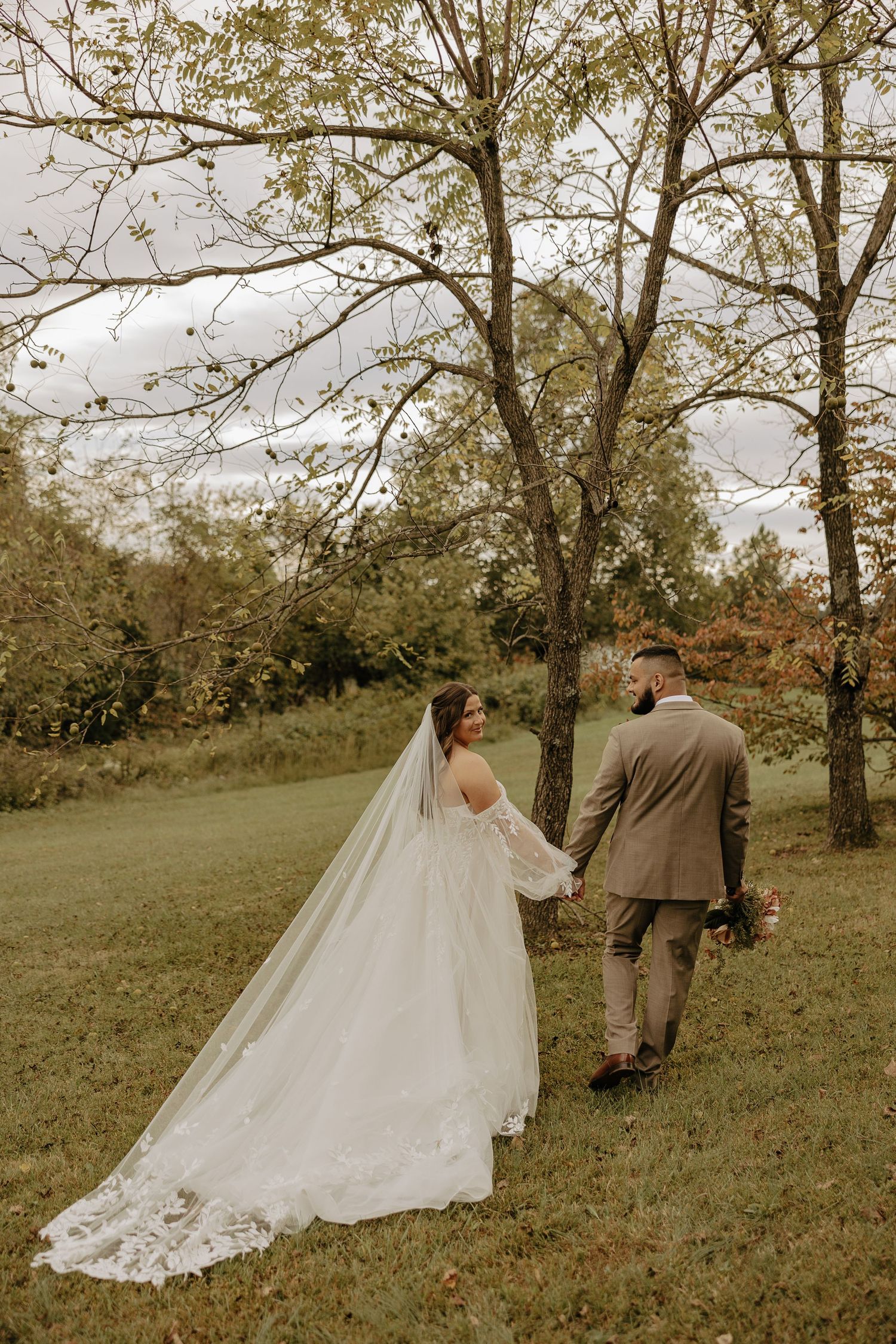 A couple walks hand in hand through a scenic autumn landscape on their wedding day.