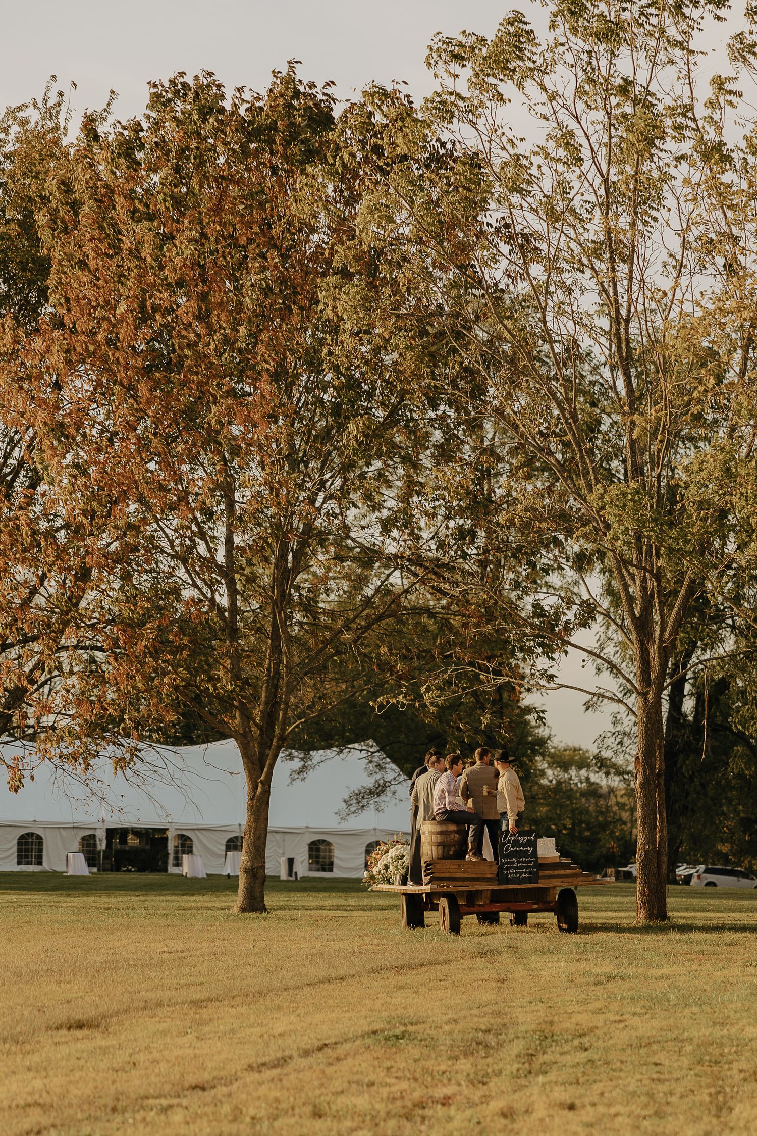 Rustic autumn landscape with trees and vintage trucks parked in a grassy field at sunset.