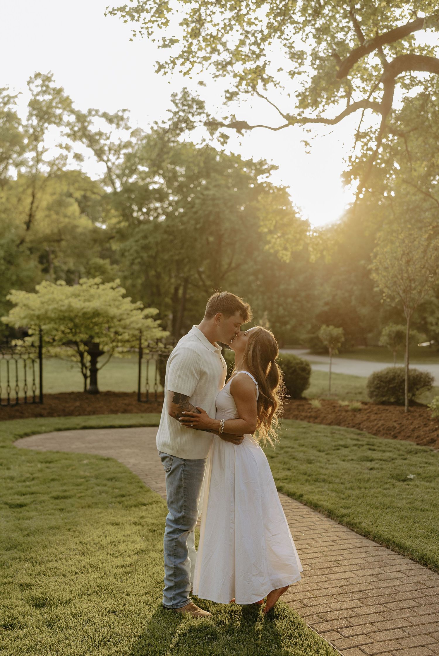 Couple sharing a romantic kiss on a brick path bathed in golden sunset light.