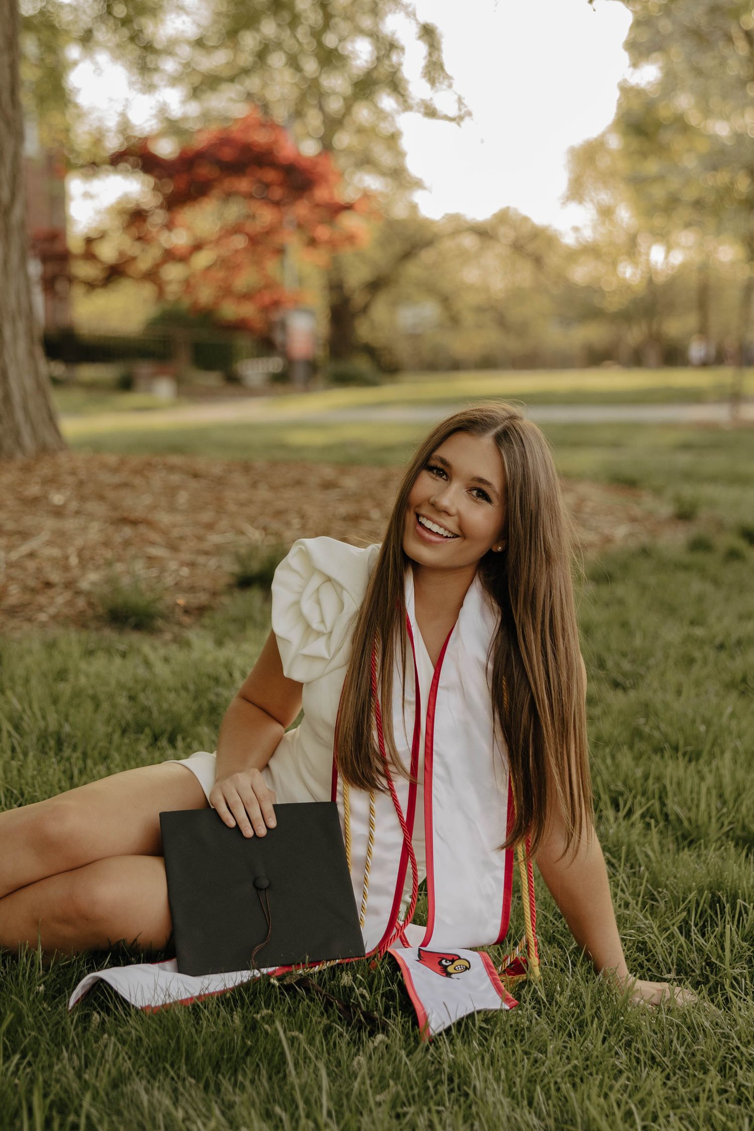 Graduate lying on grass during outdoor graduation photo session with red stoles.