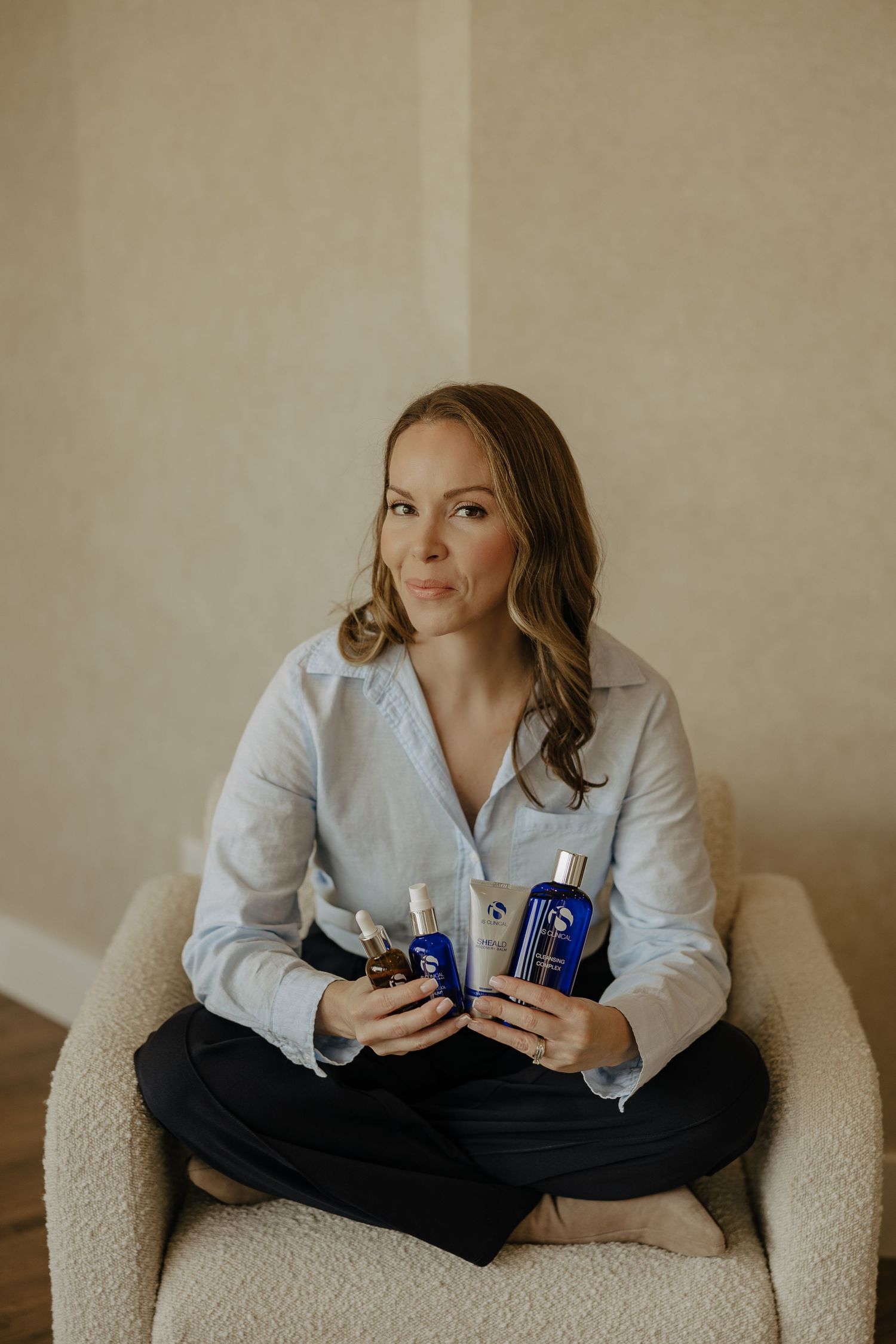 Person in white button-down shirt relaxing on cream-colored armchair with products.