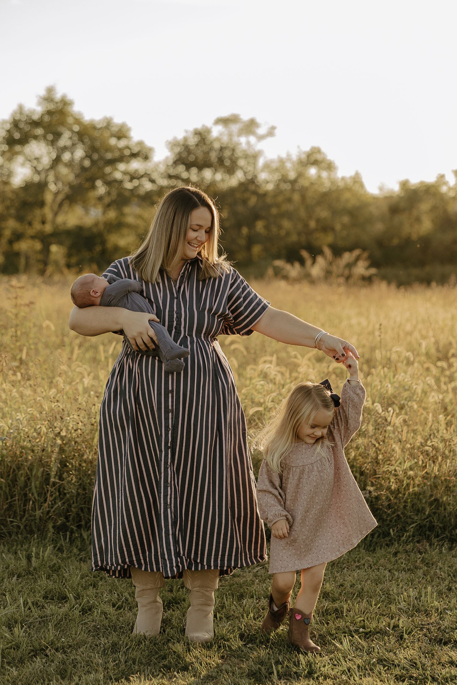 Mother and daughter dancing together in a golden meadow at sunset.