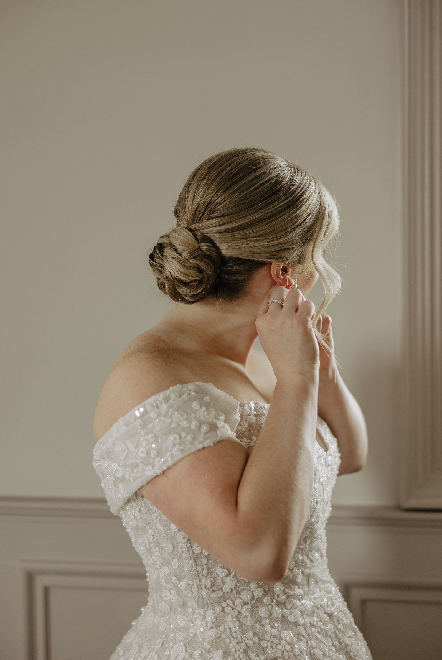 An elegant bridal updo and off-shoulder lace dress captured in soft natural light.