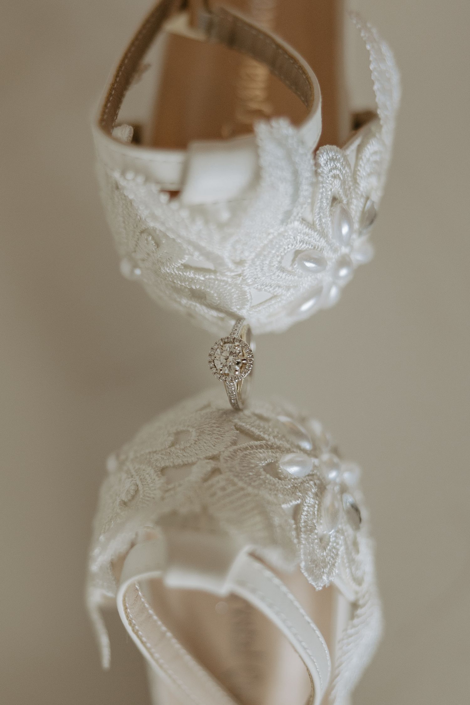 Elegant white lace bridal shoes with crystal embellishment hanging on display against neutral background.