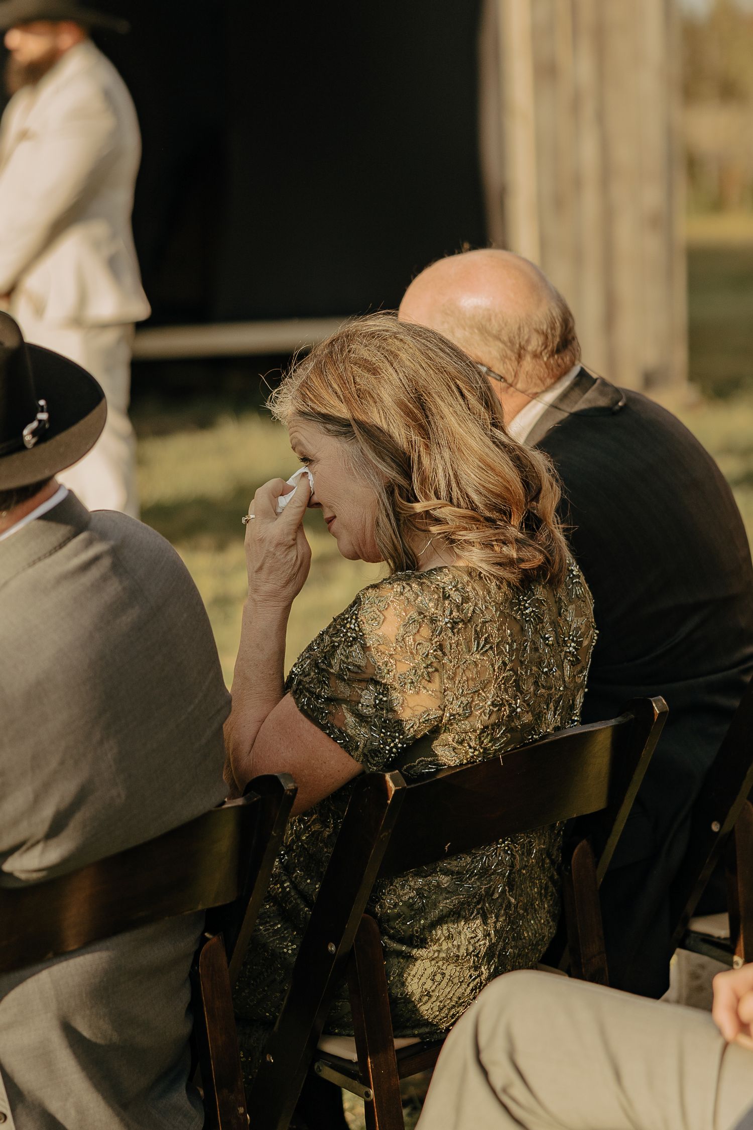 Guest in a patterned dress wipes away tears during an emotional outdoor ceremony.