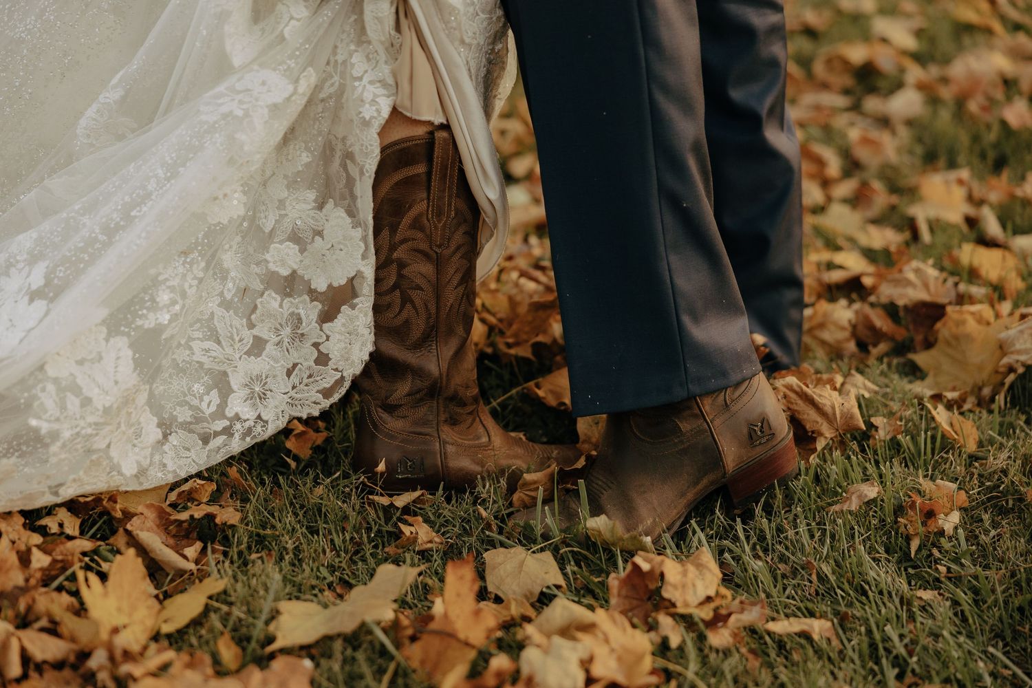 Detail shot of wedding attire and boots on grass with autumn leaves.