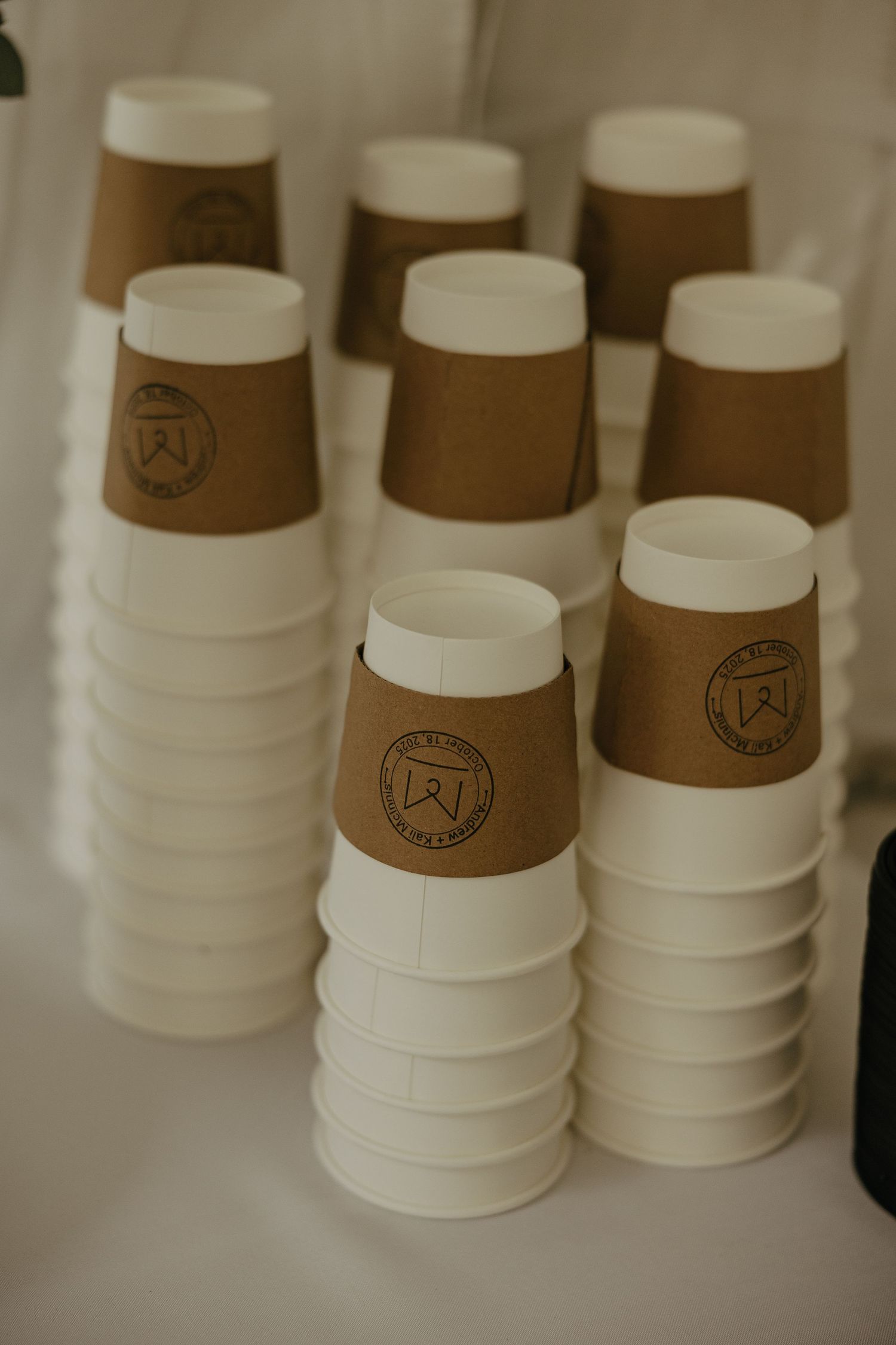 Stacked white and brown coffee cups with branded logos arranged in rows.