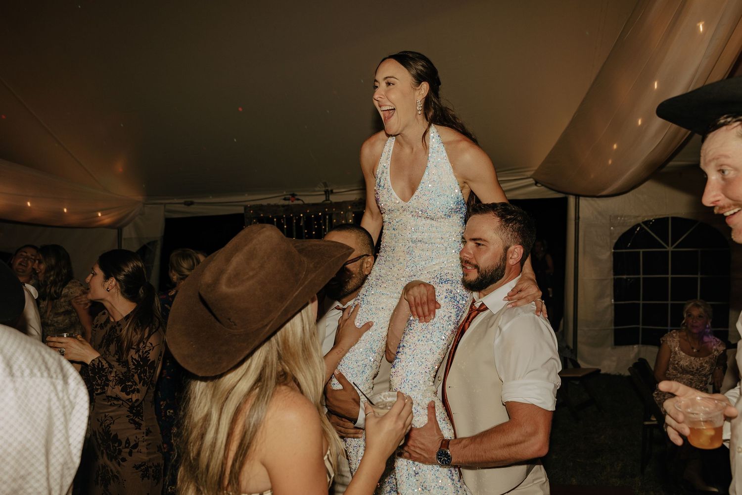 Lively wedding reception celebration under white tent with string lights.