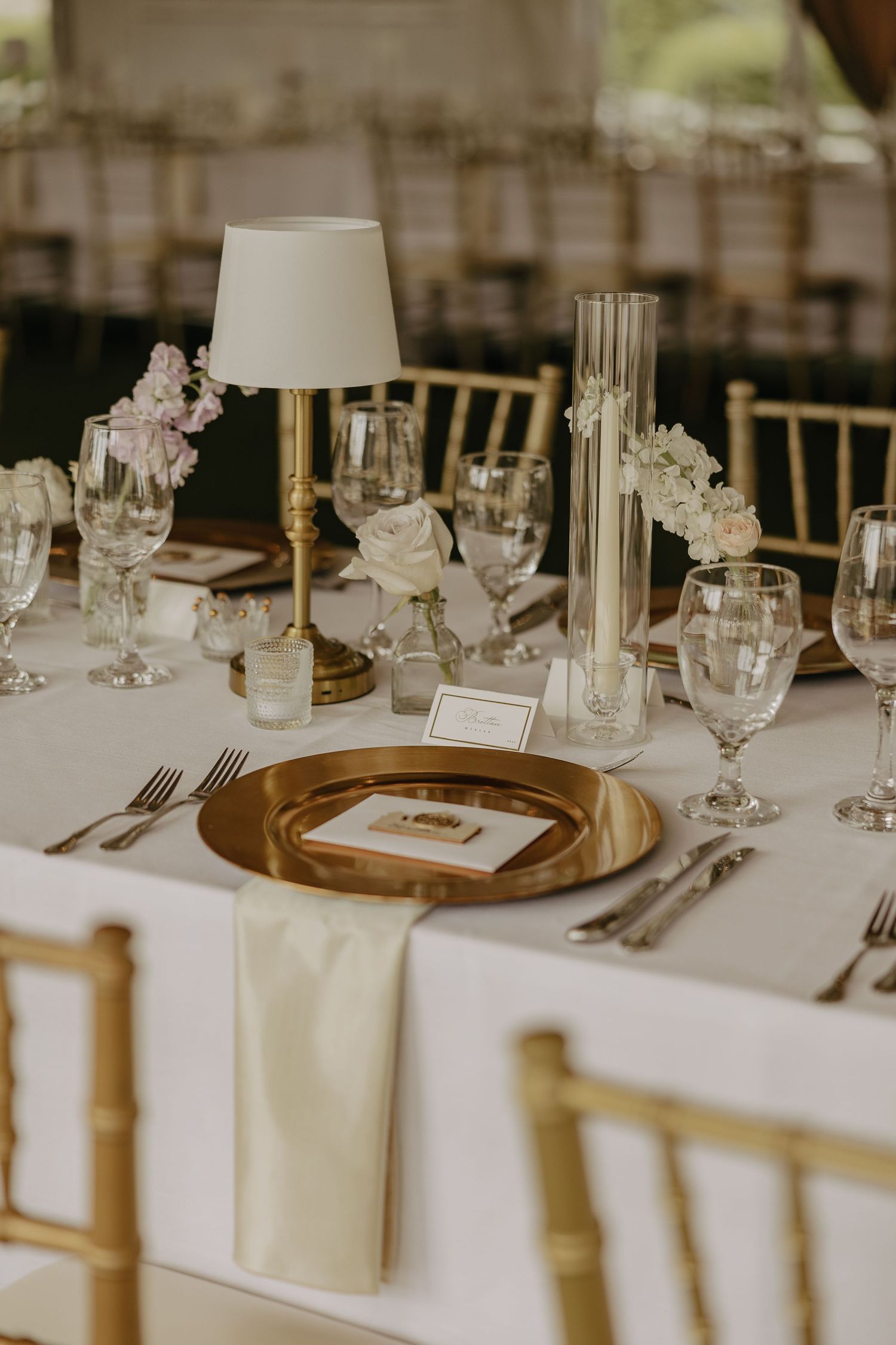 Sophisticated table setting with gold charger plates, white lampshades, and delicate floral centerpieces.