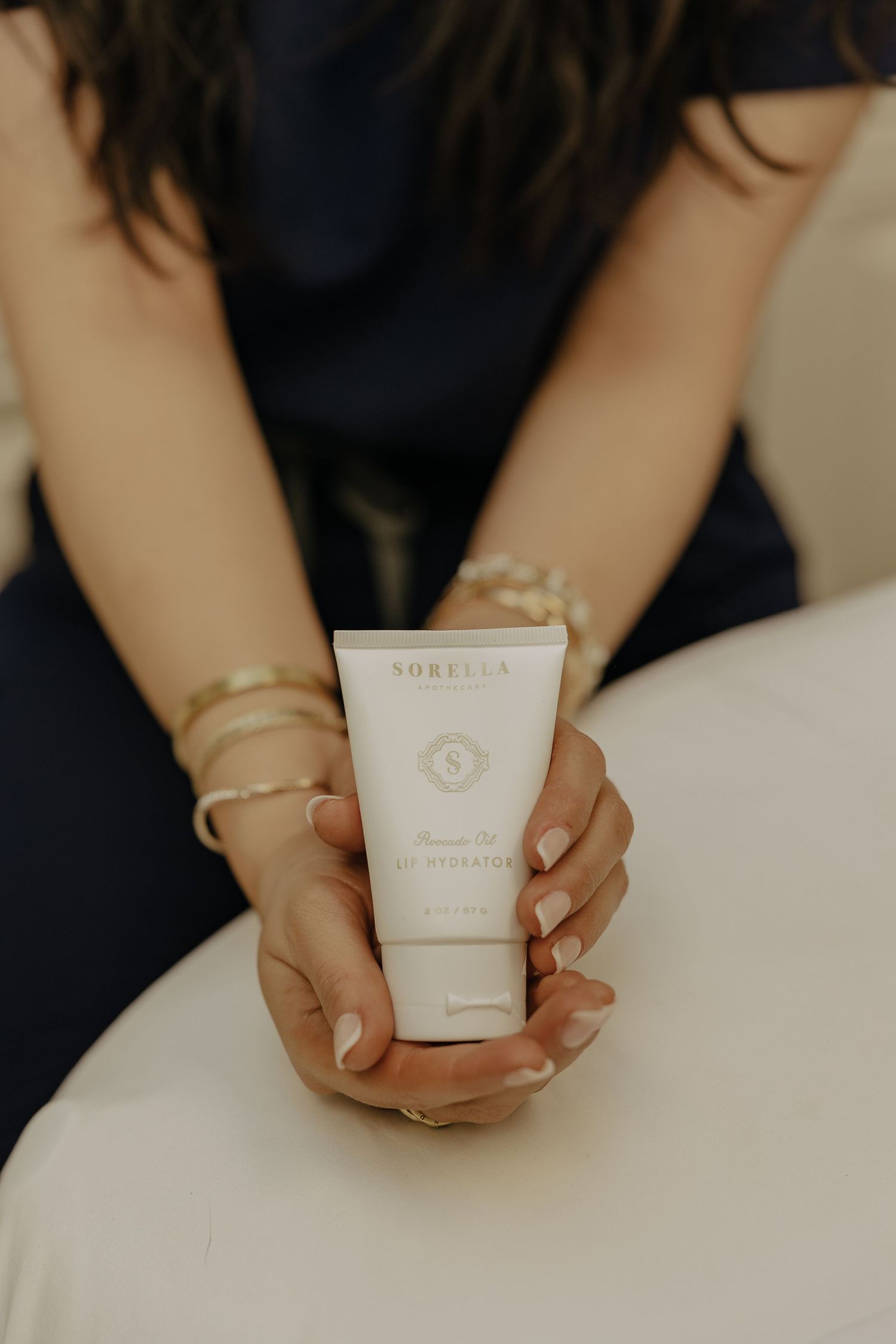 Hands holding white skincare product container against light background.