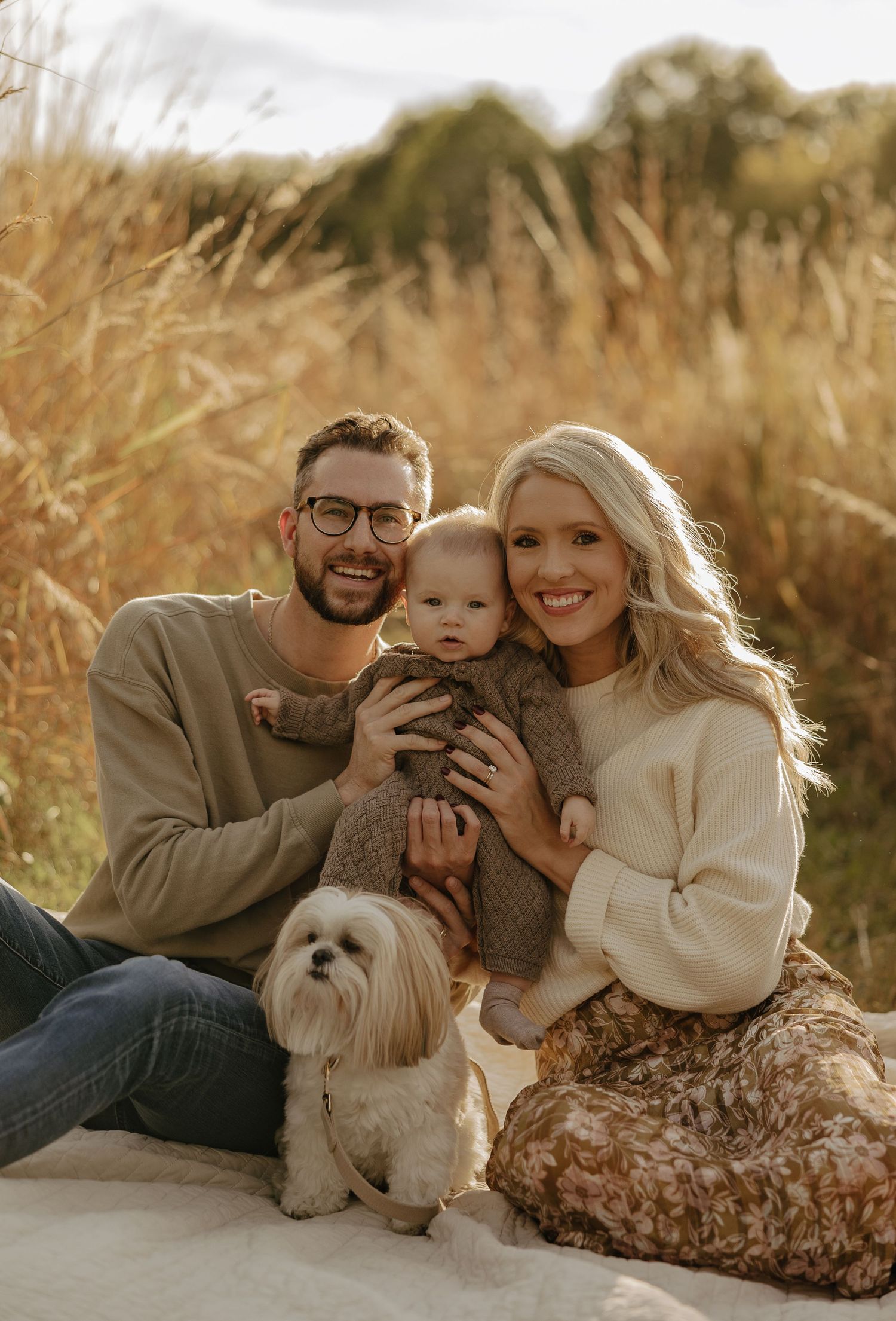 Casual outdoor family portrait with white dog on blanket during golden hour.