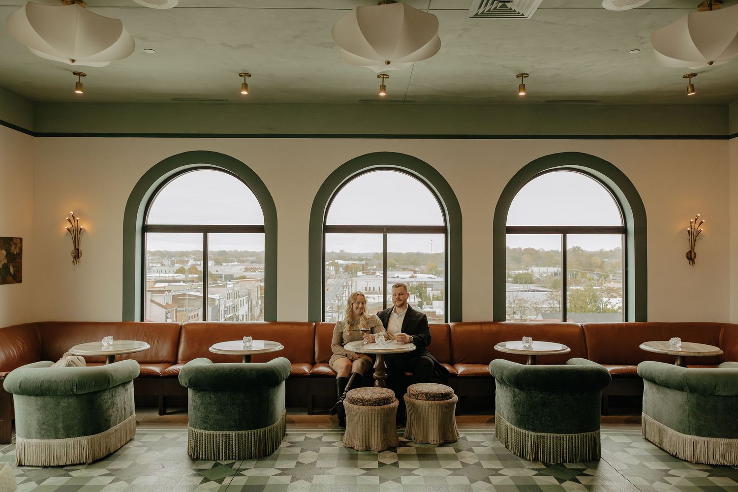 Elegant lounge area with arched windows, green velvet seating, and panoramic city views at a luxury venue.
