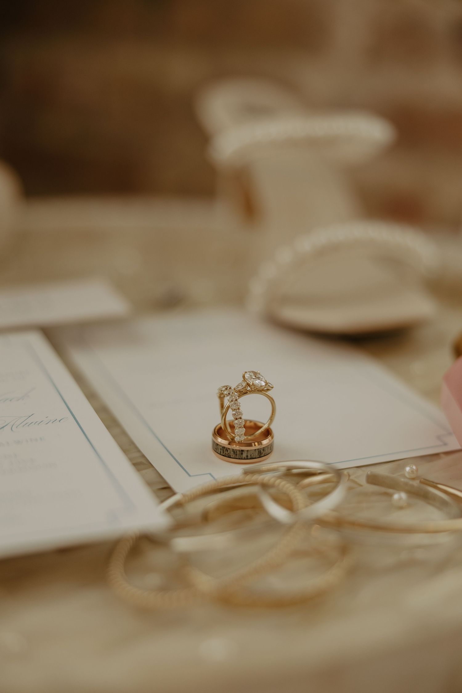 A gold engagement ring with diamonds sits elegantly on white paper in a soft sepia-toned lighting.