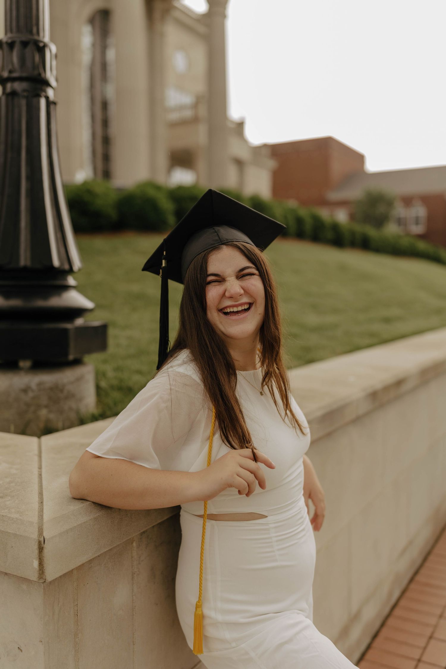 Graduate in cap and gown smiles joyfully outside classical building.