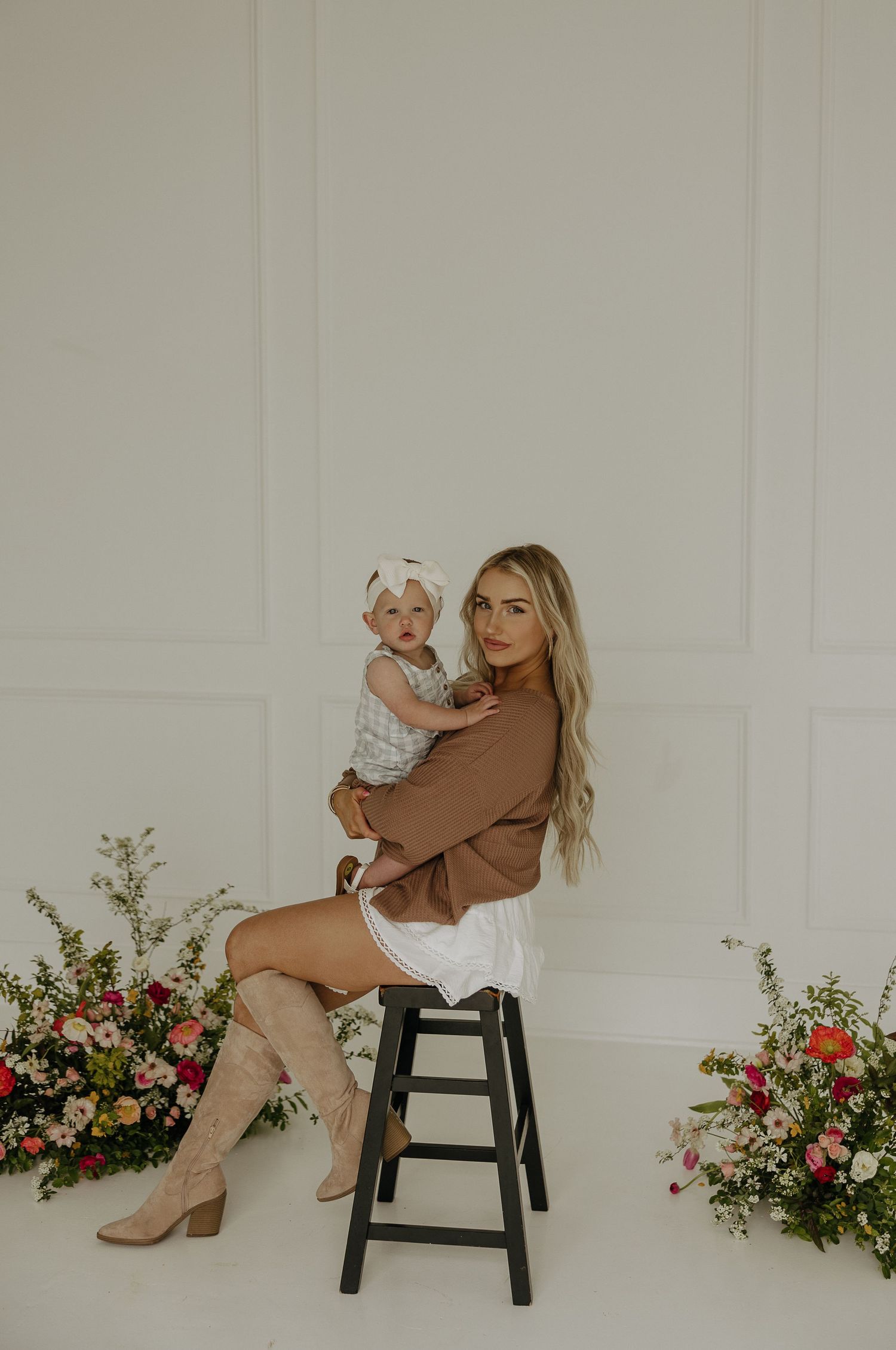 Studio photoshoot with floral arrangements and black stool against white backdrop.