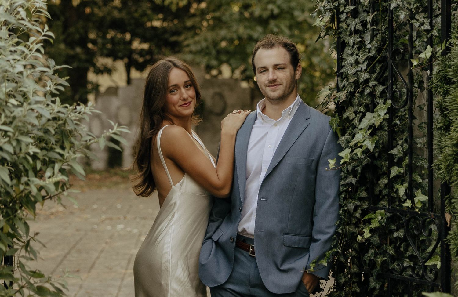 A couple laughs together on a garden path surrounded by greenery.