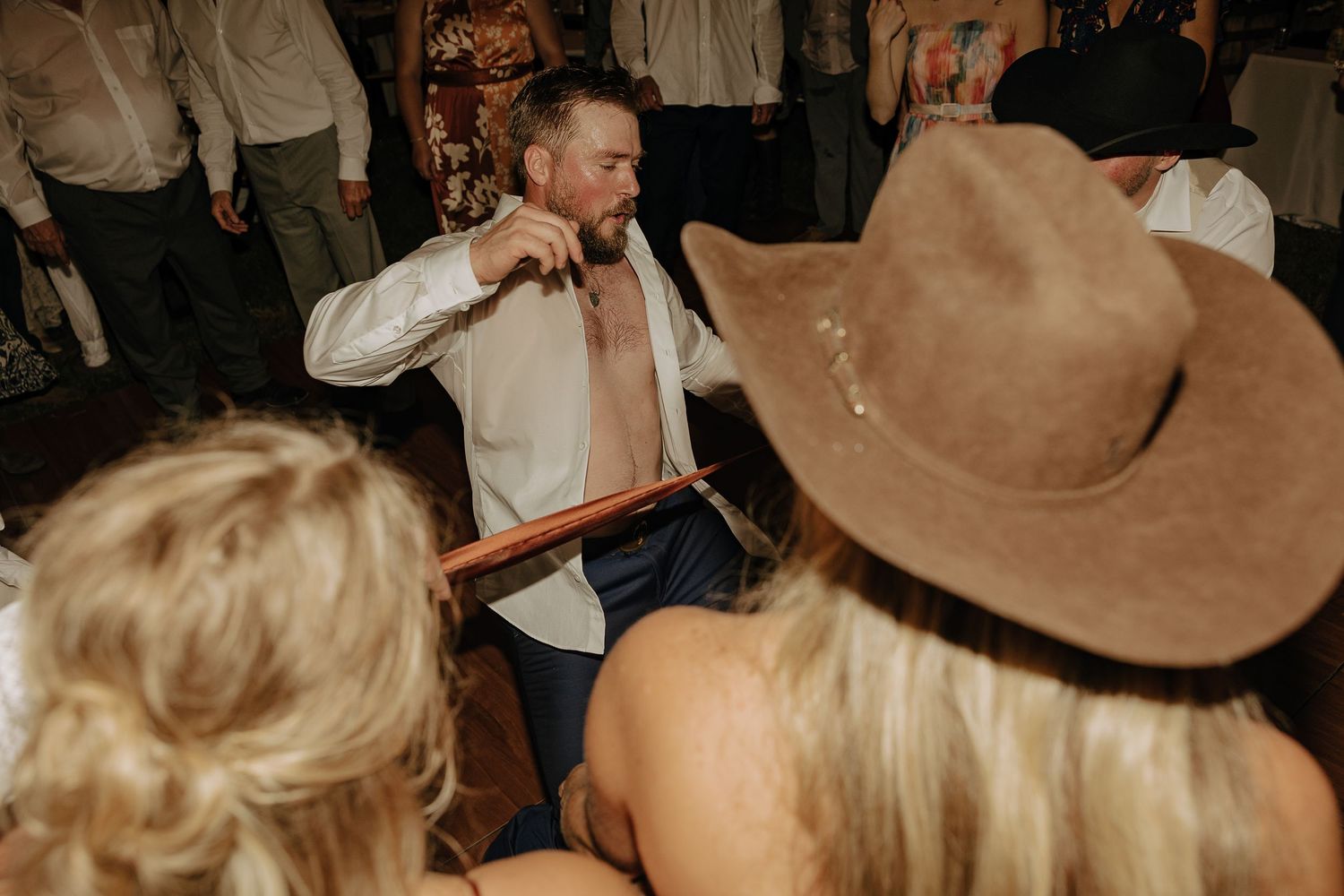 Wedding guests wearing cowboy hats celebrate on a crowded dance floor.